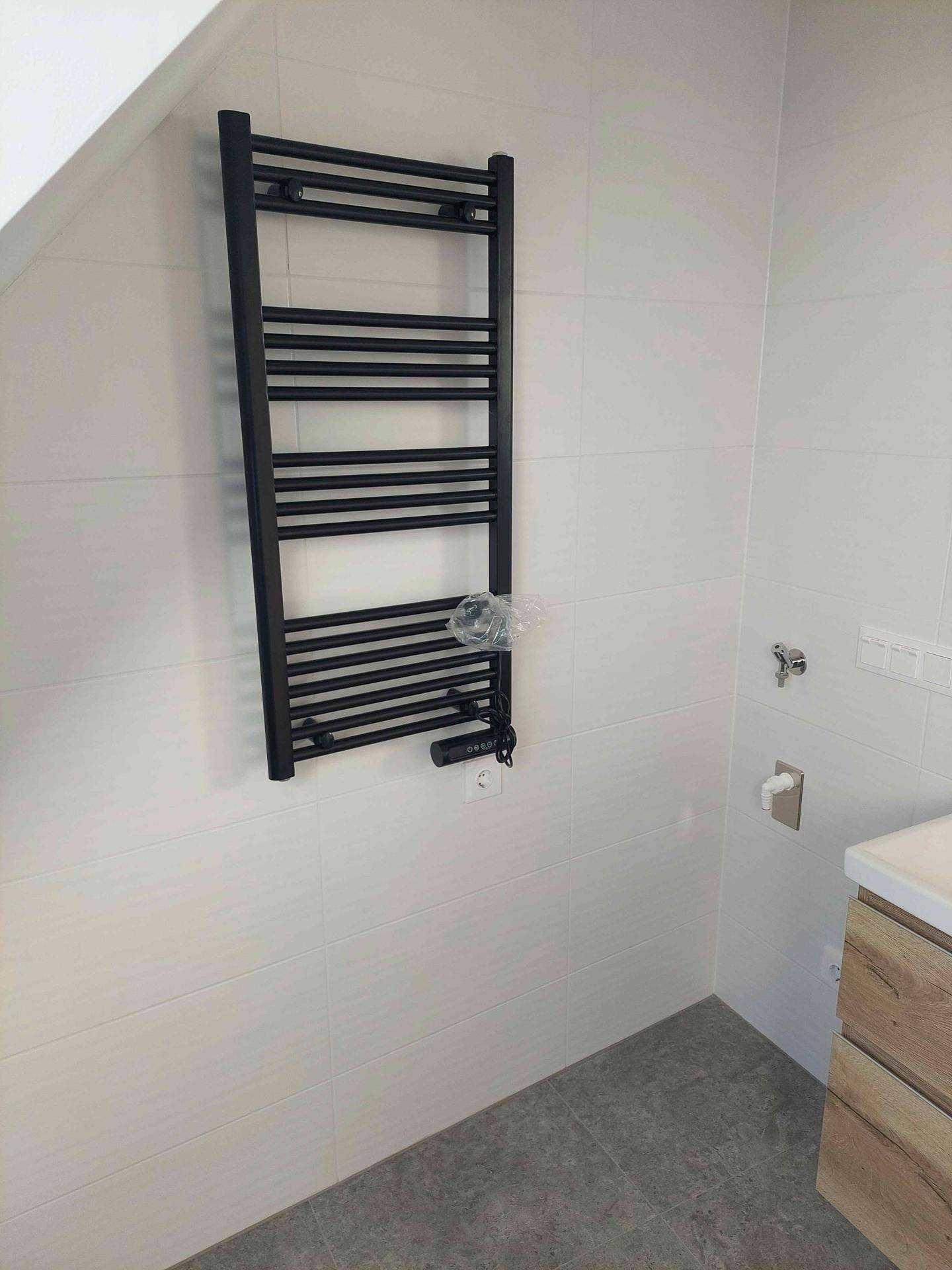 Badezimmer mit schwarzem Handtuchheizkörper, weißen Wandfliesen und praktischer Dachschräge.