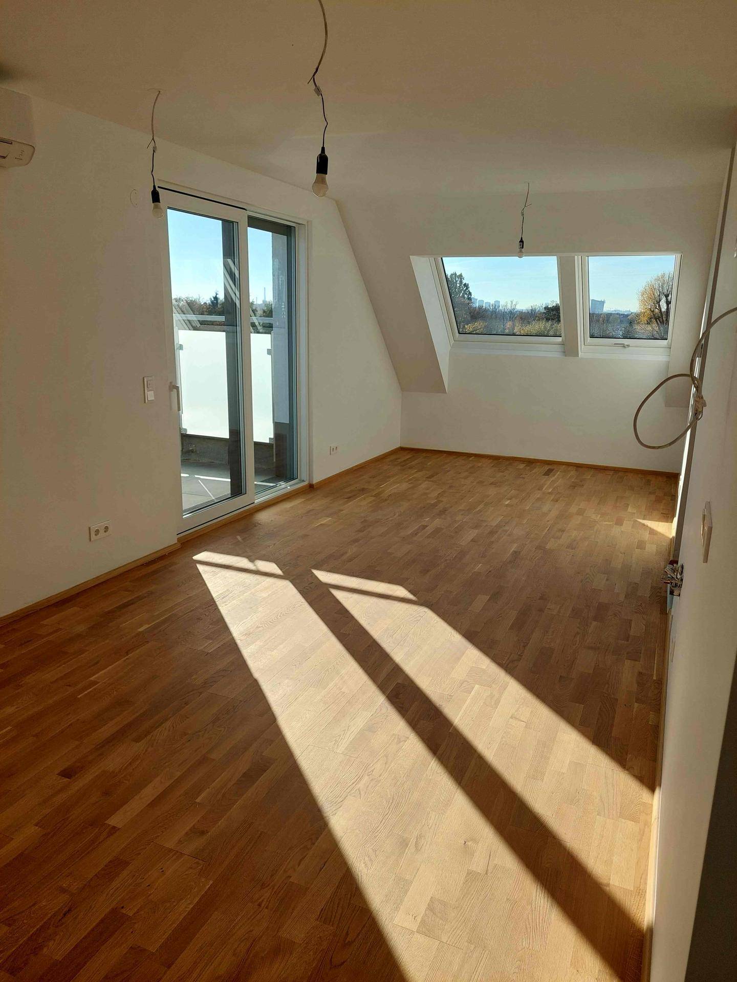 Heller Wohnraum mit Holzboden, Dachschrägen und Zugang zu einer Terrasse, durchflutet von Sonnenlicht.