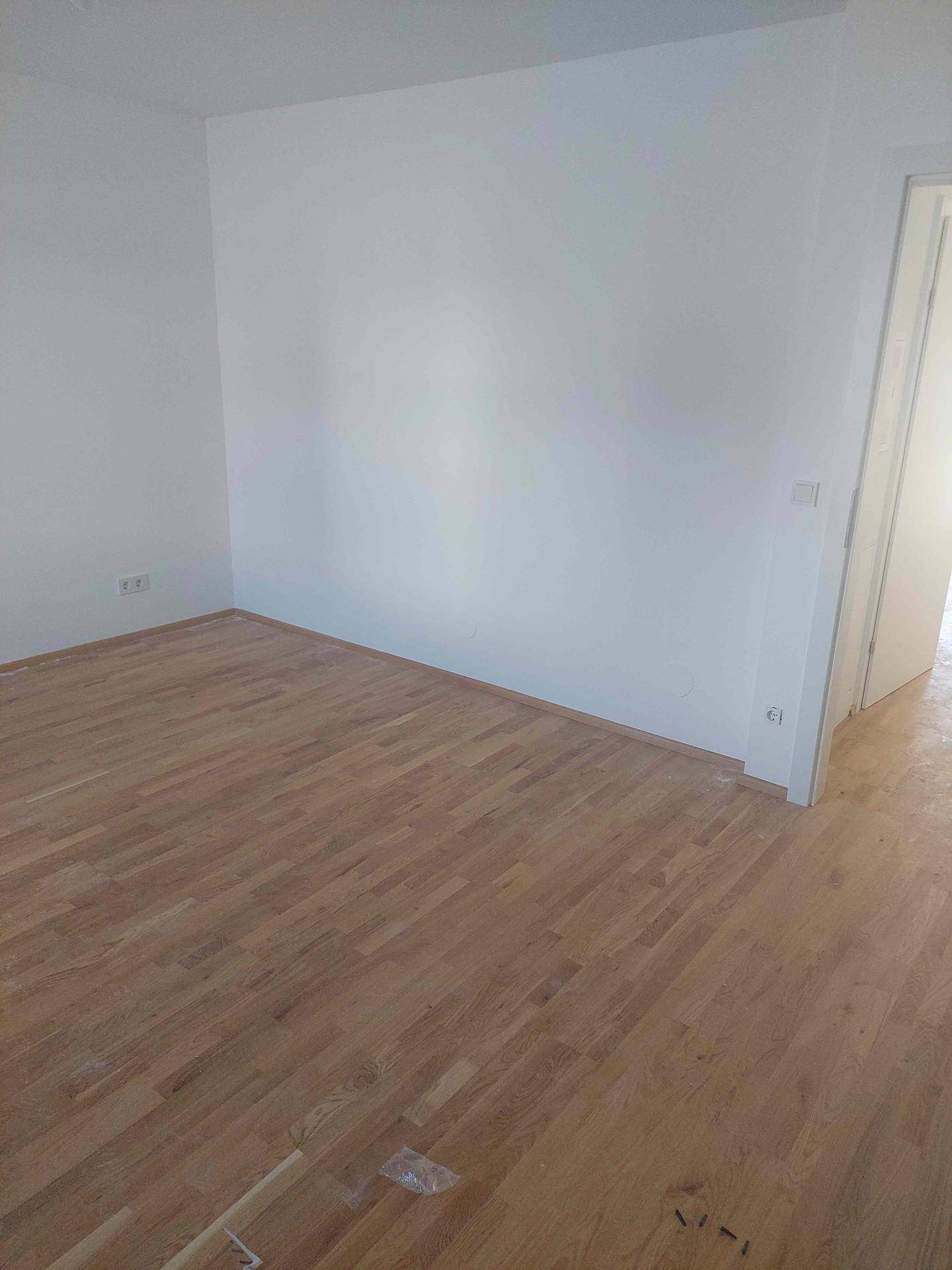 Leerer Raum mit frisch verlegtem Holzparkettboden und weißen Wänden, bereit für die Einrichtung.