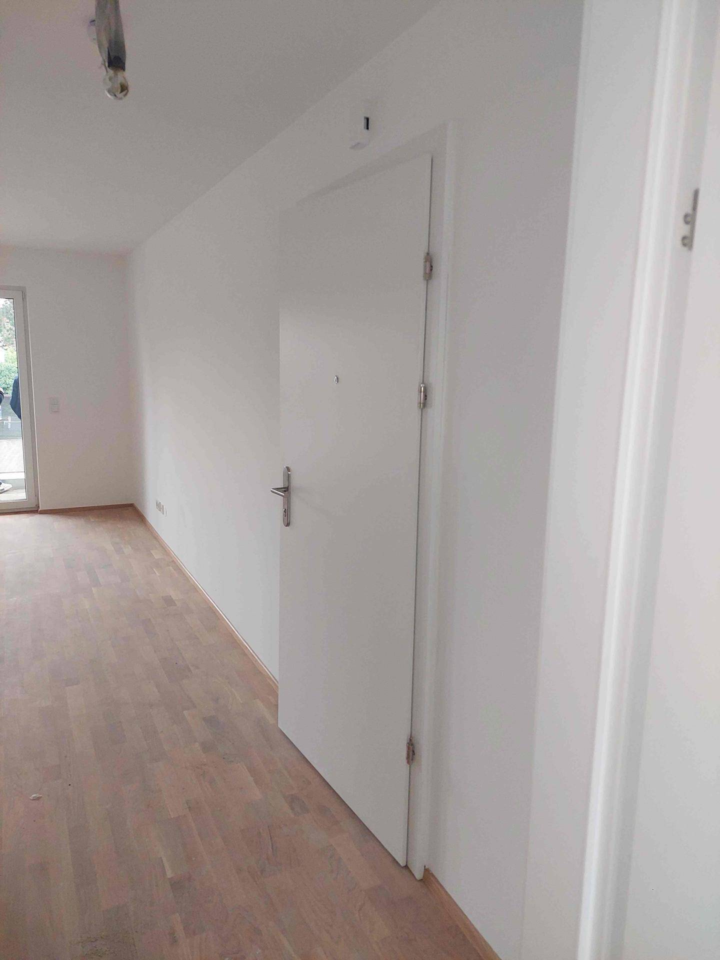 Heller Flur mit Holzplankenboden und weißer Eingangstür, die zu weiteren Räumen führt.