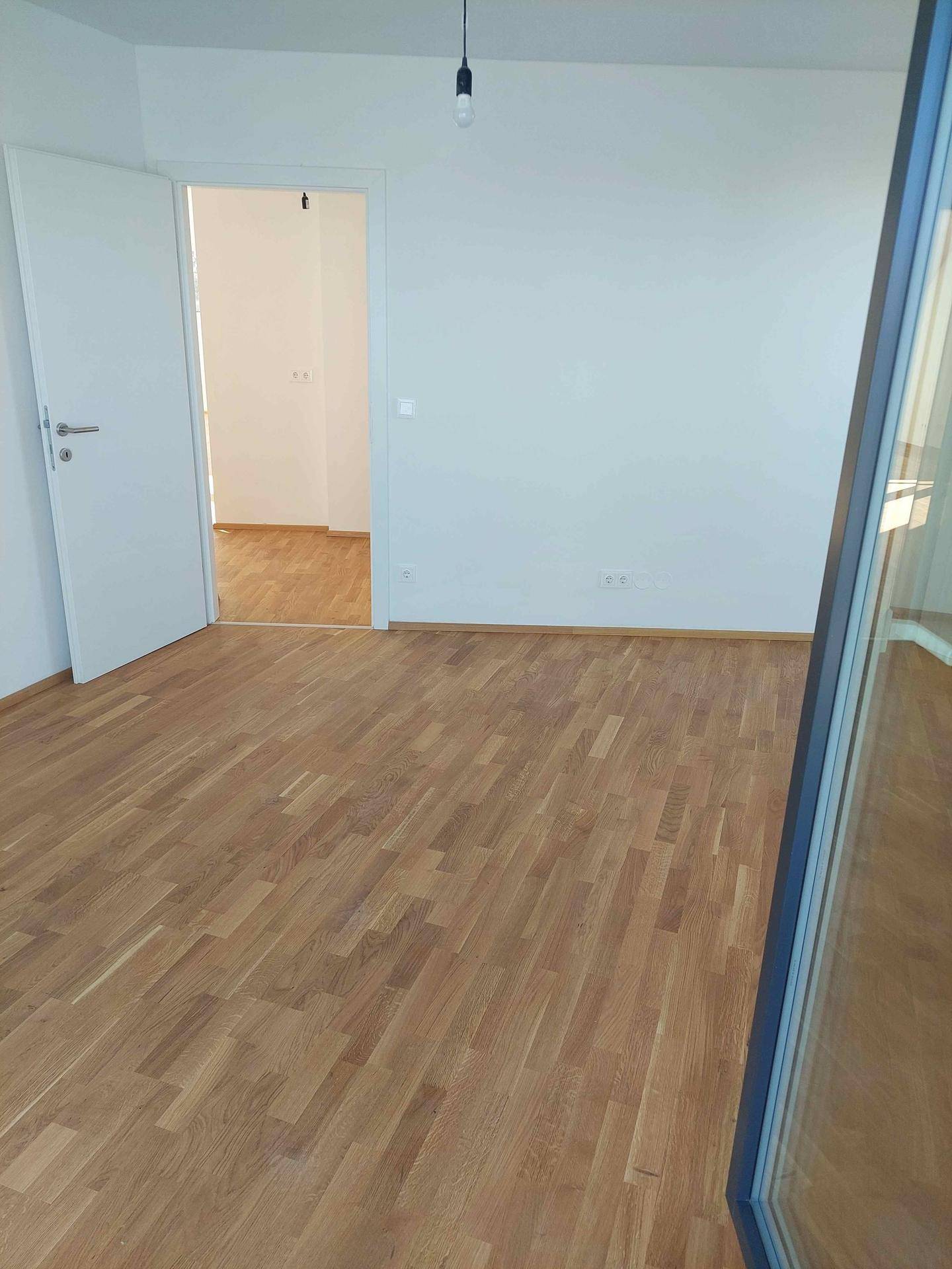 Leeres Zimmer mit Holzboden und weiß gestrichenen Wänden, bereit für individuelle Gestaltung.