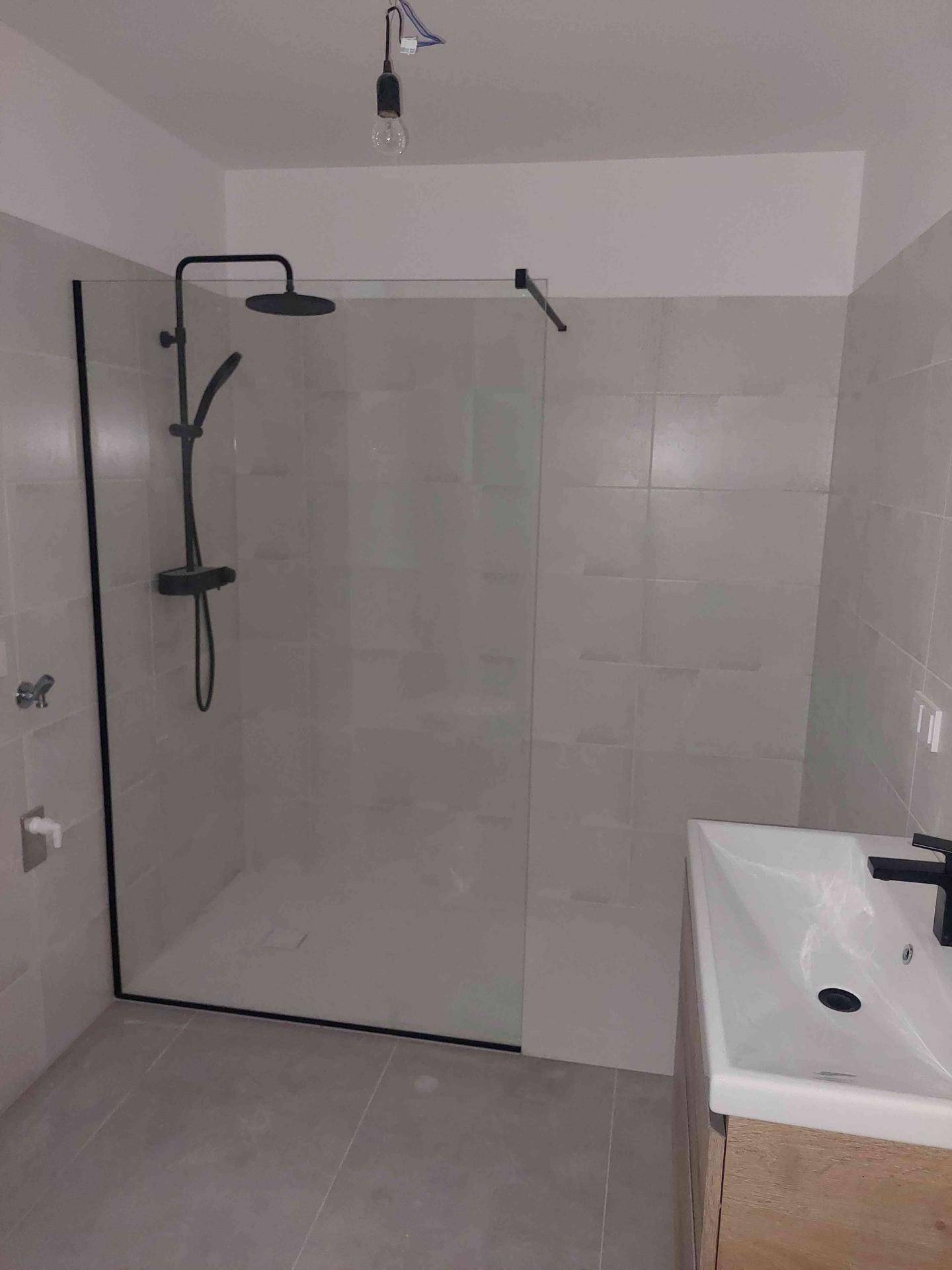 Modernes Badezimmer mit begehbarer Dusche, grauen Fliesen und schwarzer Armatur am Waschbecken.