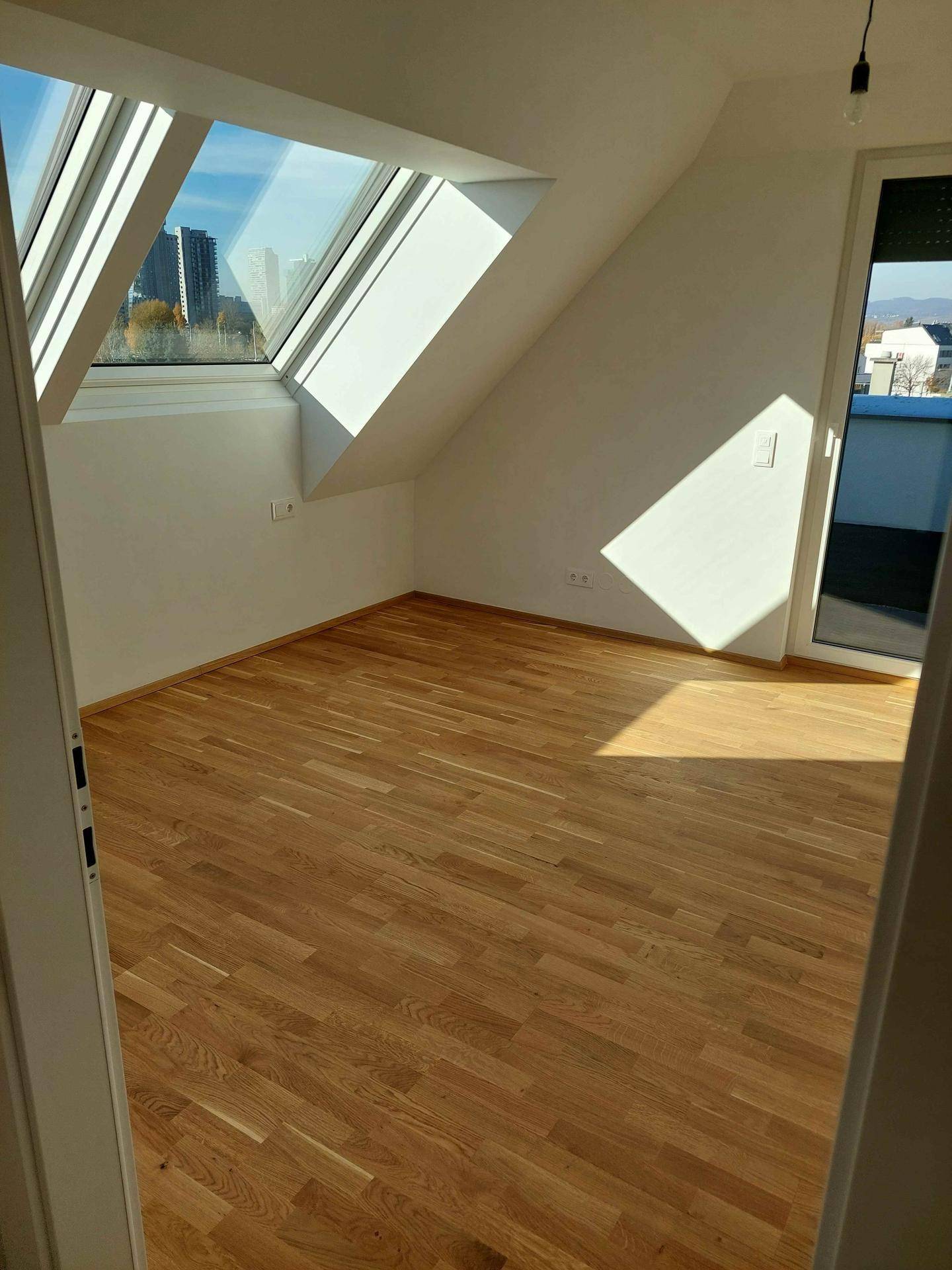 Helles Zimmer mit Holzboden, Dachschrägen und einem großen Dachfenster, das viel Licht spendet.