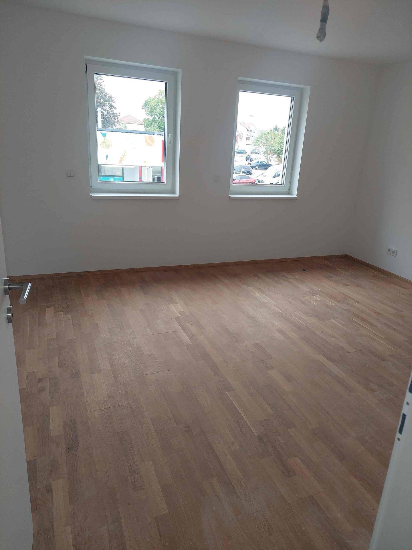 Helles Schlafzimmer mit zwei Fenstern, neuem Holzplankenboden und weißen Wänden.