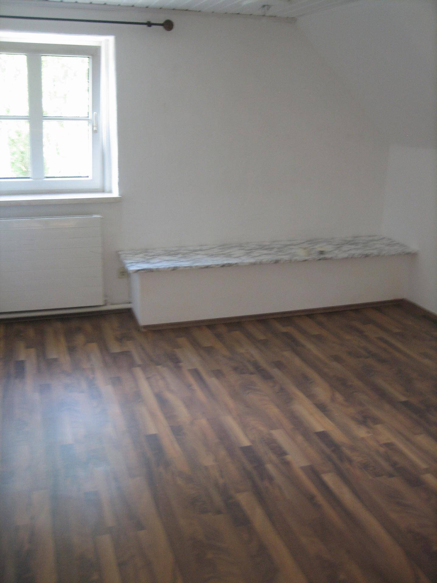 Helles Zimmer mit Laminatboden, Fenster und Heizkörper, ideal als Schlaf- oder Gästezimmer.