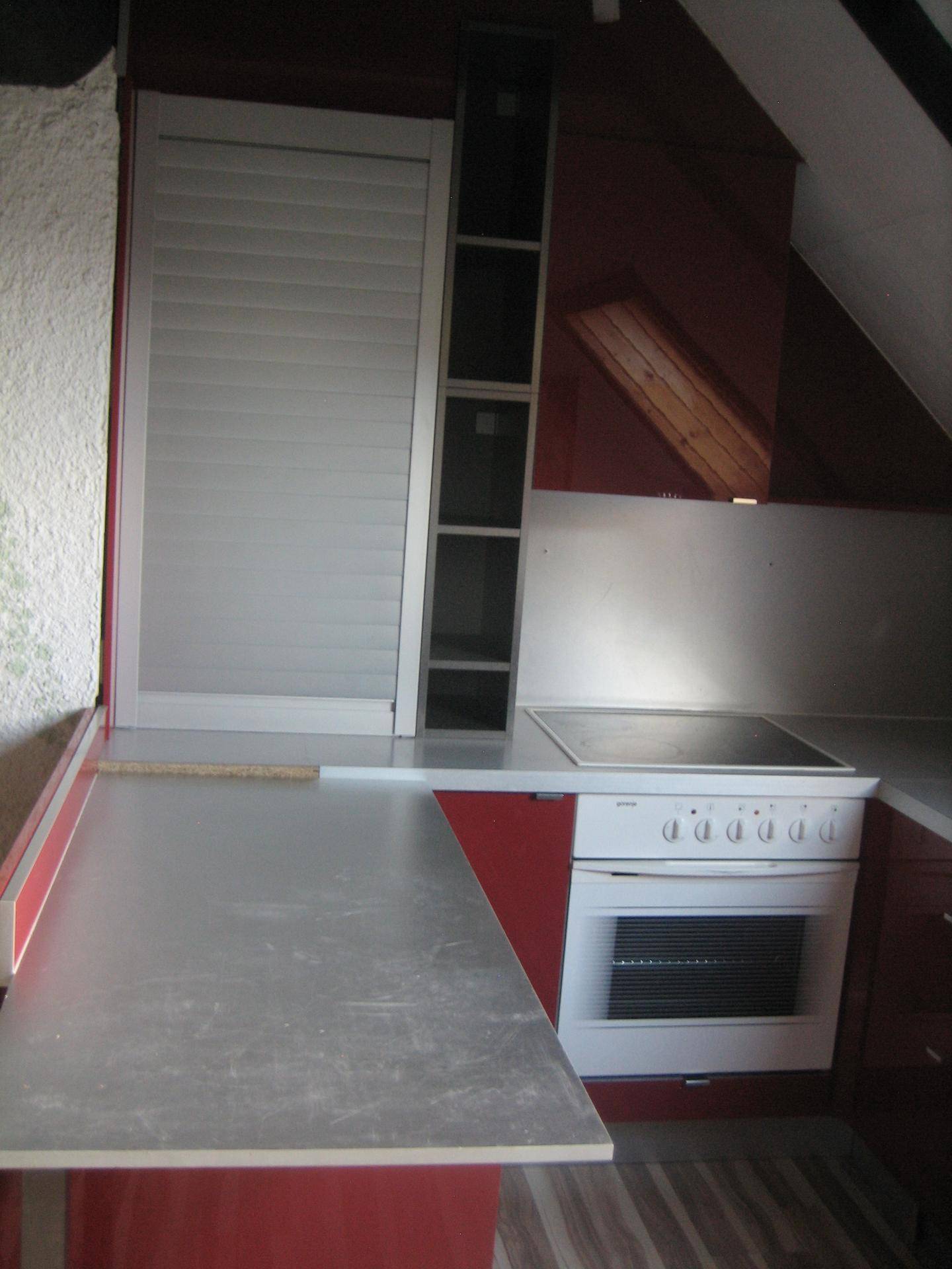 Dachgeschossküche mit roter Front, Kochfeld und Rollladenschrank für zusätzlichen Stauraum.