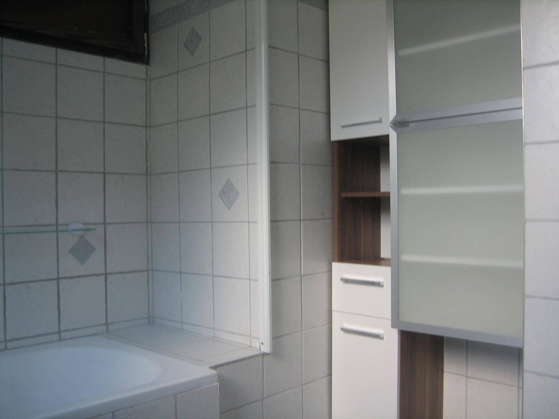 Badezimmer mit weißen Fliesen, Badewanne und praktischen Hängeschränken für Stauraum.