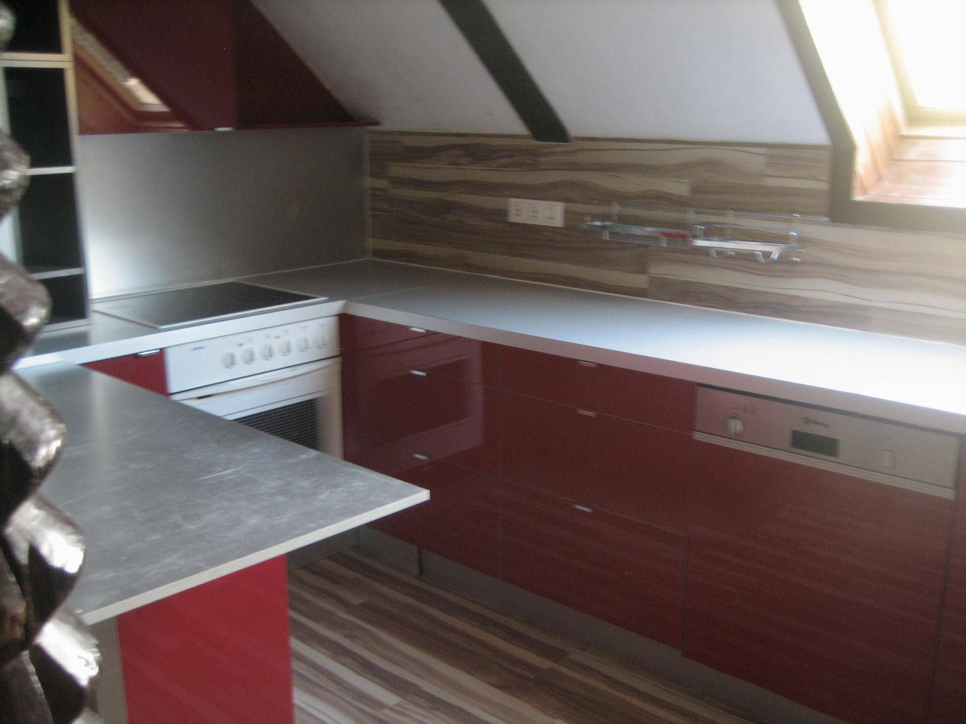 Dachgeschossküche mit roter Front, Kochfeld, Backofen und Holzwandverkleidung.