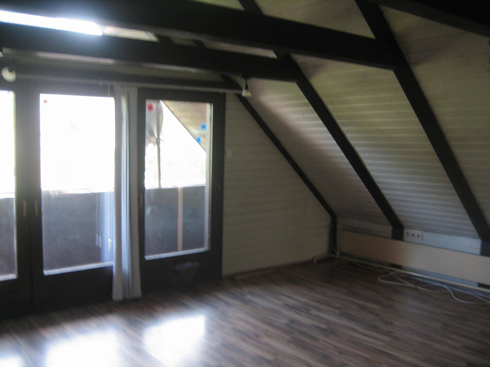 Heller Wohnbereich im Dachgeschoss mit Holzbalken, Laminatboden und Zugang zum Balkon.