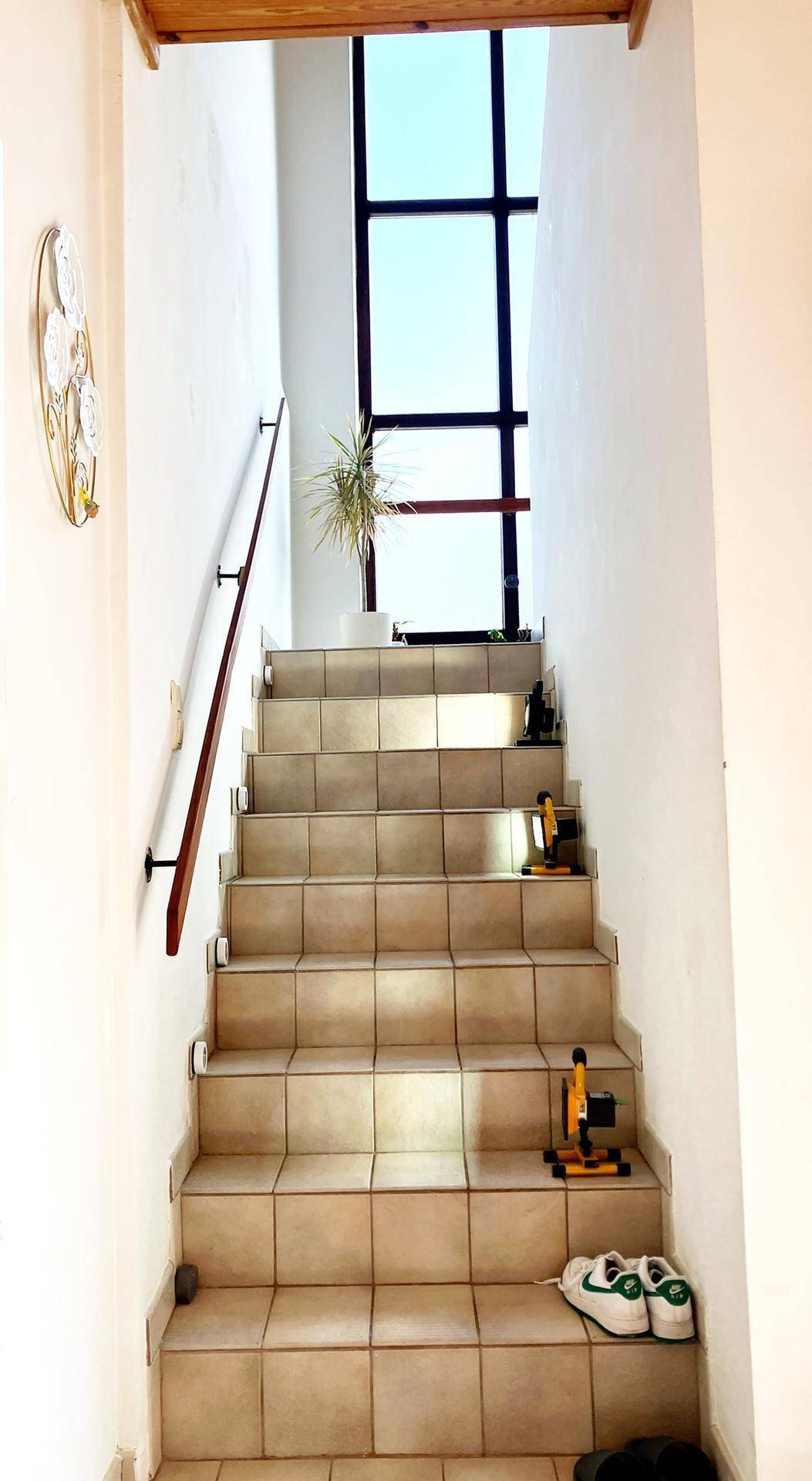 Helle Treppe mit Fliesenstufen, Holzgeländer und einem hohen Fenster für viel Tageslicht.