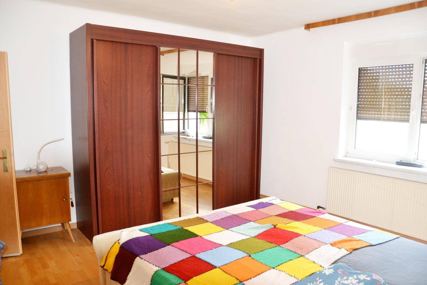 Schlafzimmer mit großem Holzschrank, Spiegeln und einem farbenfrohen Bettüberwurf.