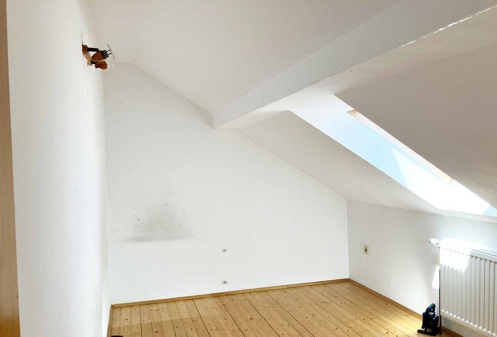 Dachzimmer mit Holzdielenboden, weiß gestrichenen Wänden und Dachfenster.