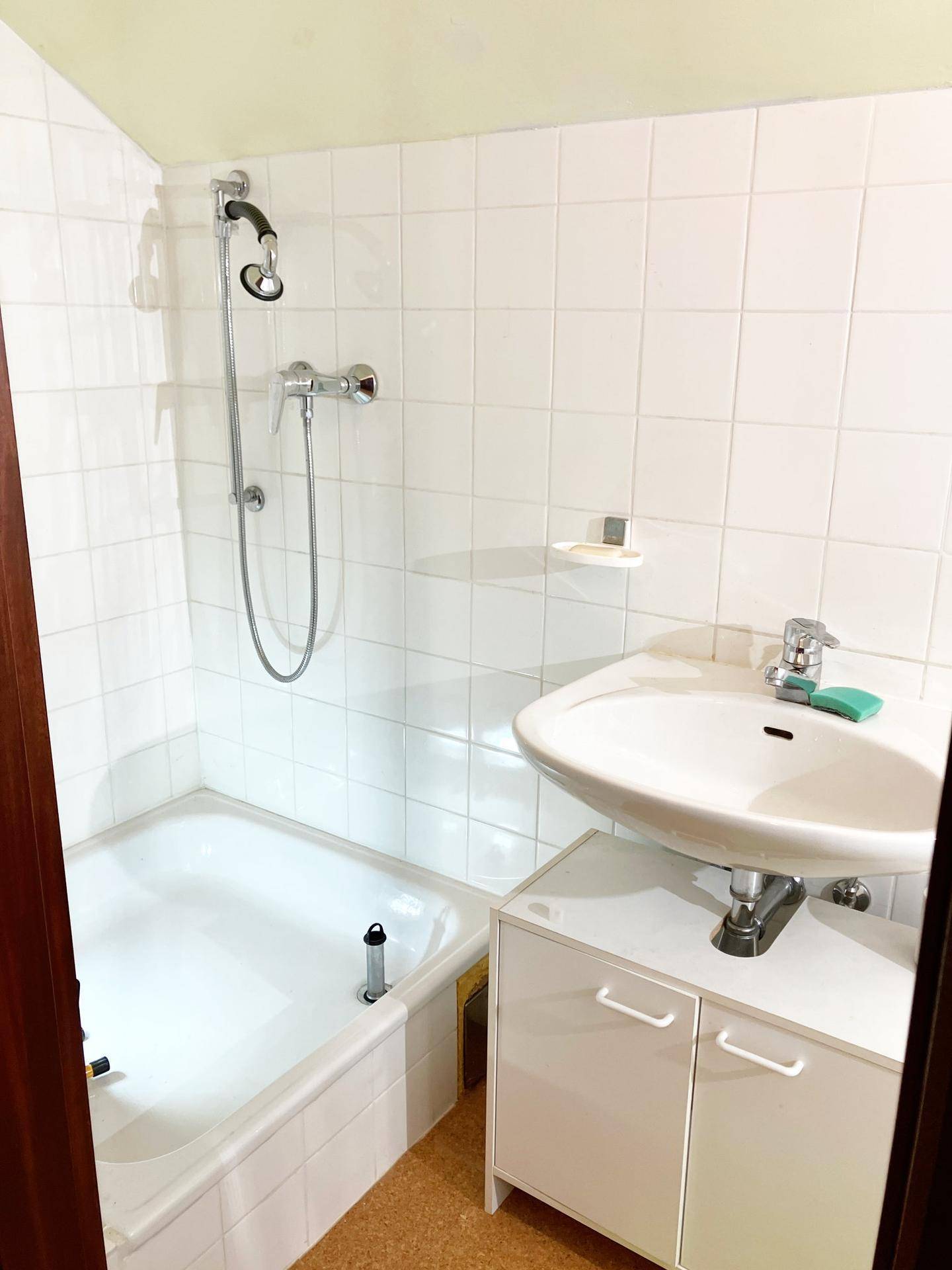 Kleines Badezimmer mit Badewanne, Duschfunktion und Waschbecken.