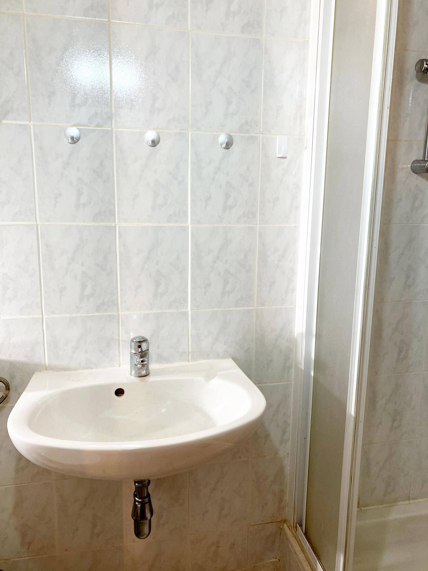 Badezimmer mit weiß gefliesten Wänden, einem Waschbecken und Duschkabine.