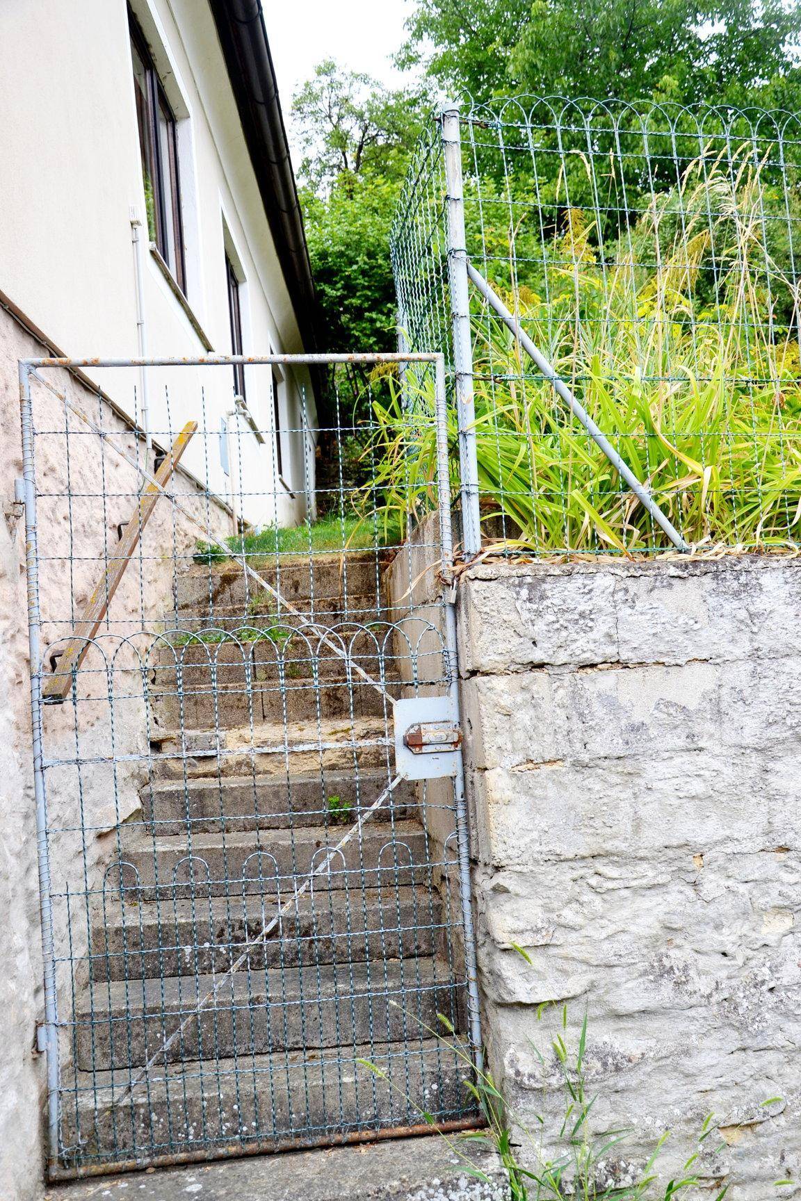 Außentreppe mit Metalltor und Zaun, umgeben von üppigem Grün.