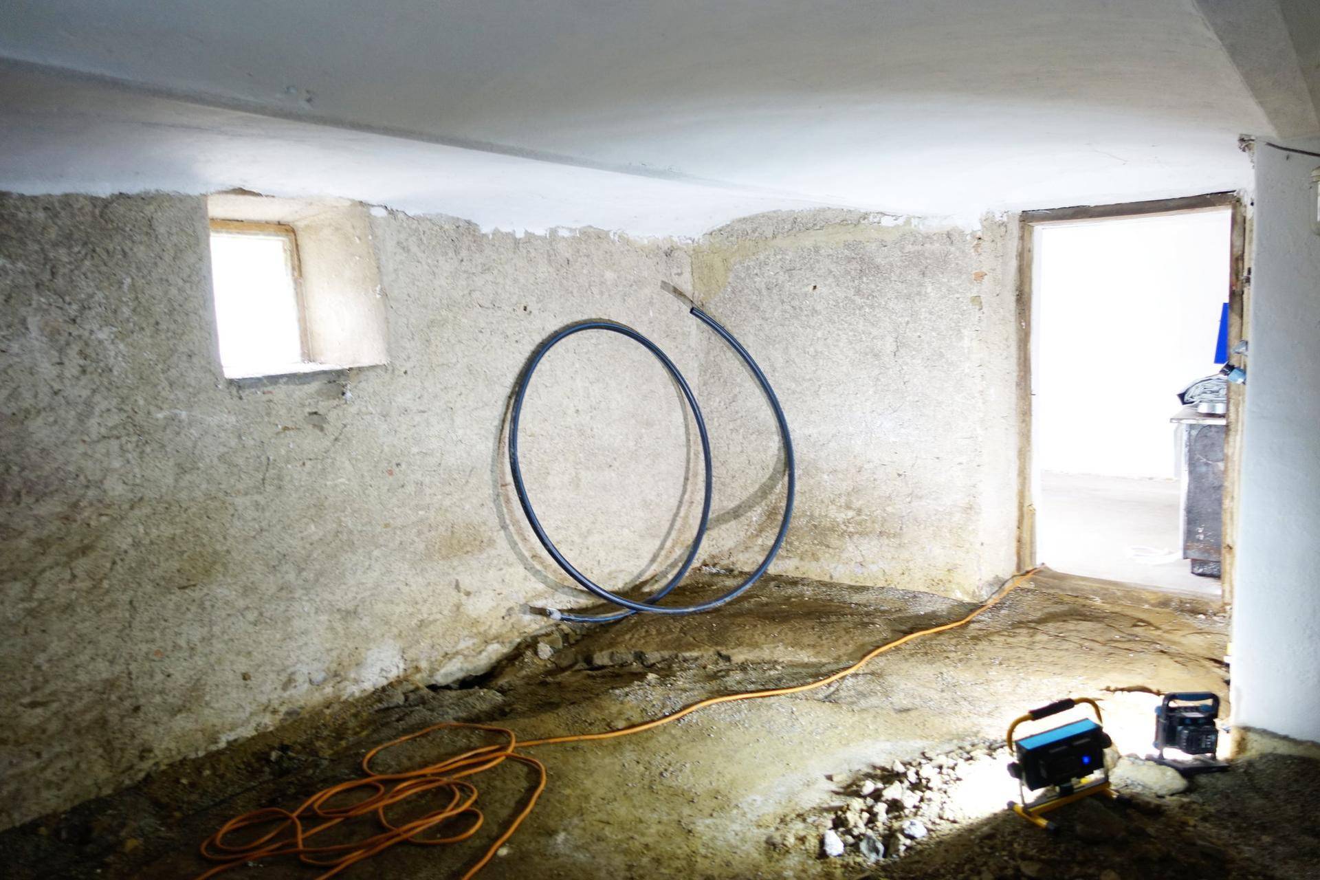 Unfertiger Kellerraum mit rauen Wänden und Installationsrohren.
