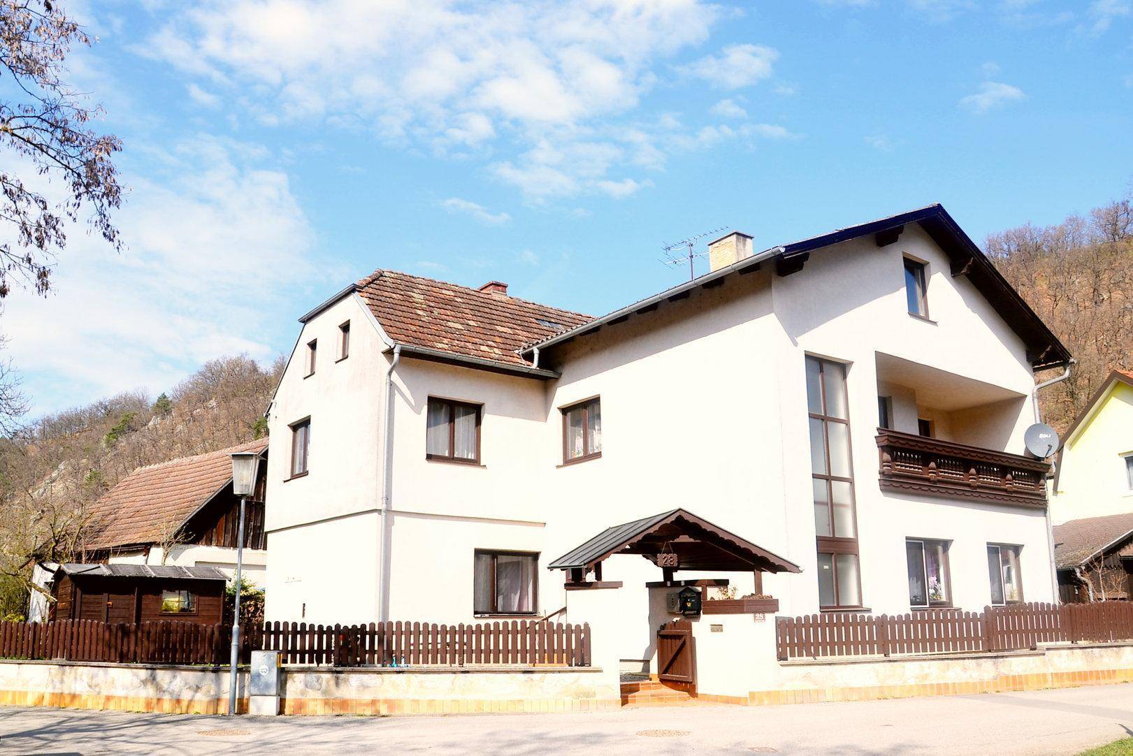 Freistehendes Haus mit weißer Fassade, Satteldach und überdachtem Eingang, umgeben von Natur.