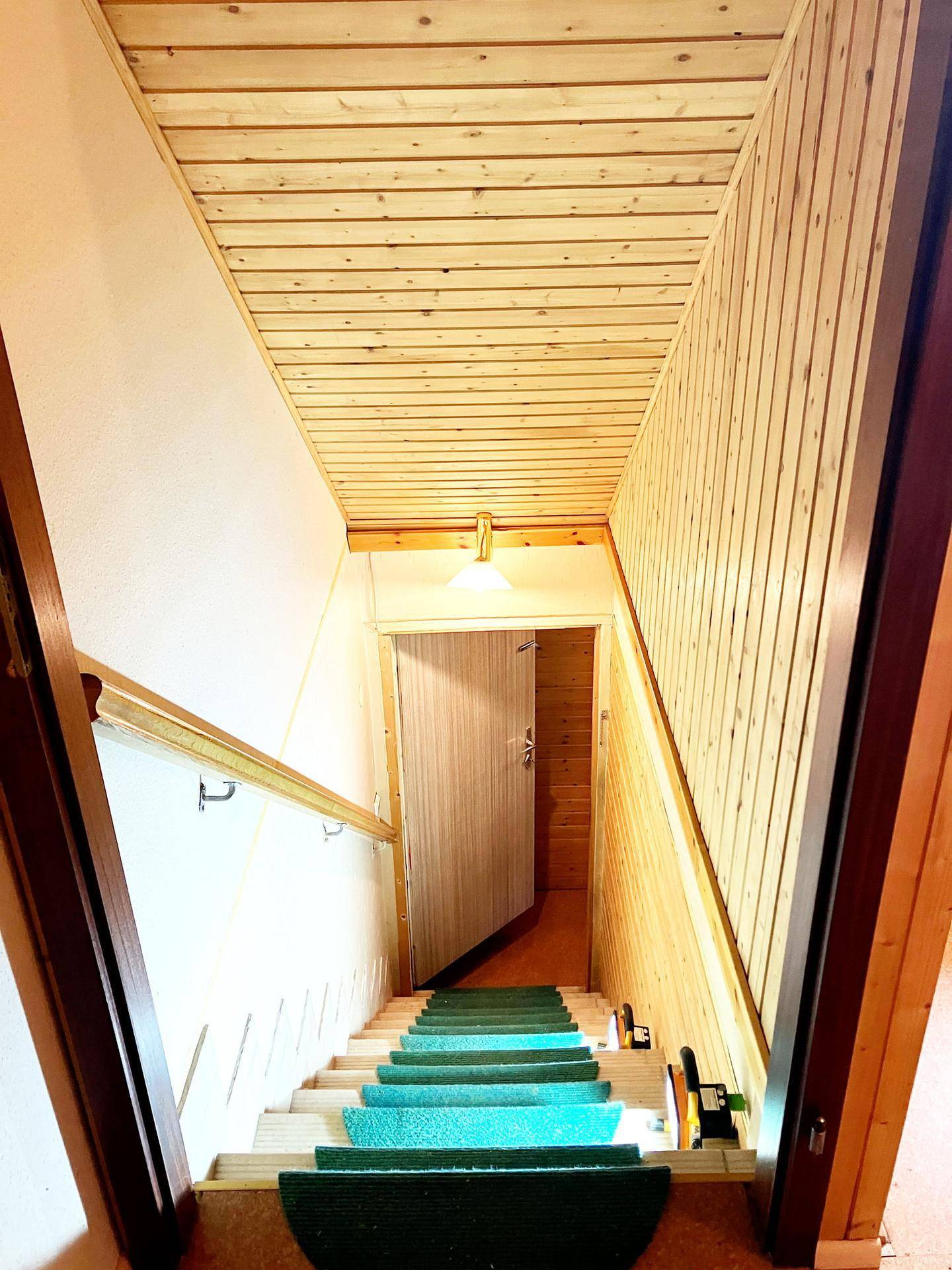 Treppenhaus mit Holzverkleidung und grünen Teppichläufern, führt zu einem weiteren Raum.
