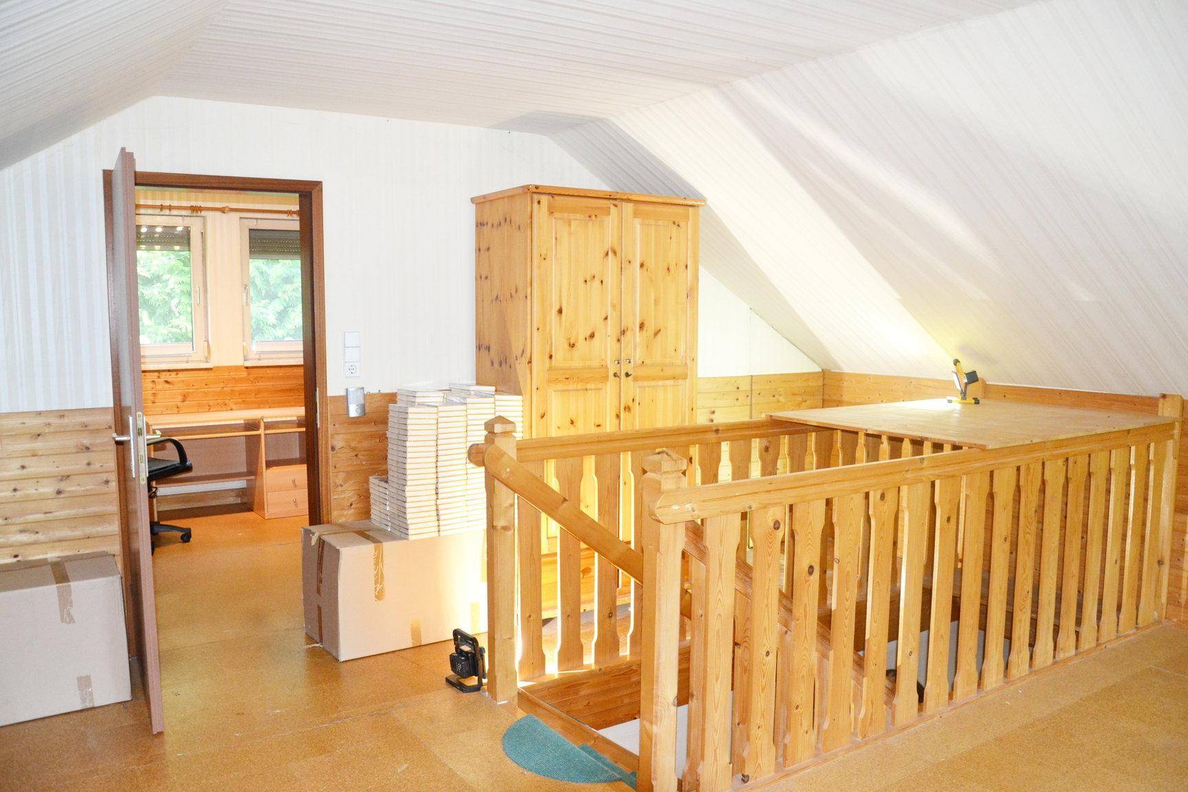 Offener Bereich im Obergeschoss mit Holzgeländer und Blick in ein angrenzendes Zimmer.