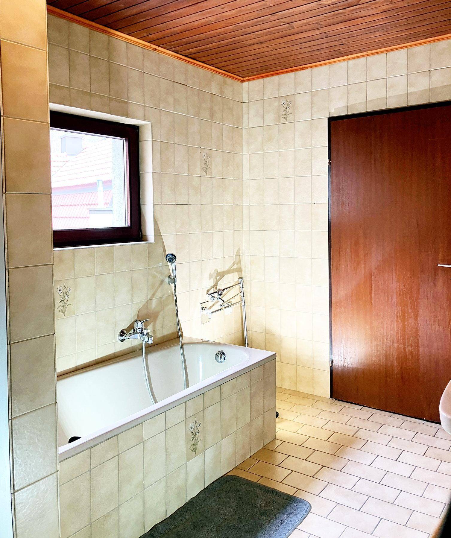 Badezimmer mit Badewanne, Fenster und beigefarbenen Wand- und Bodenfliesen.