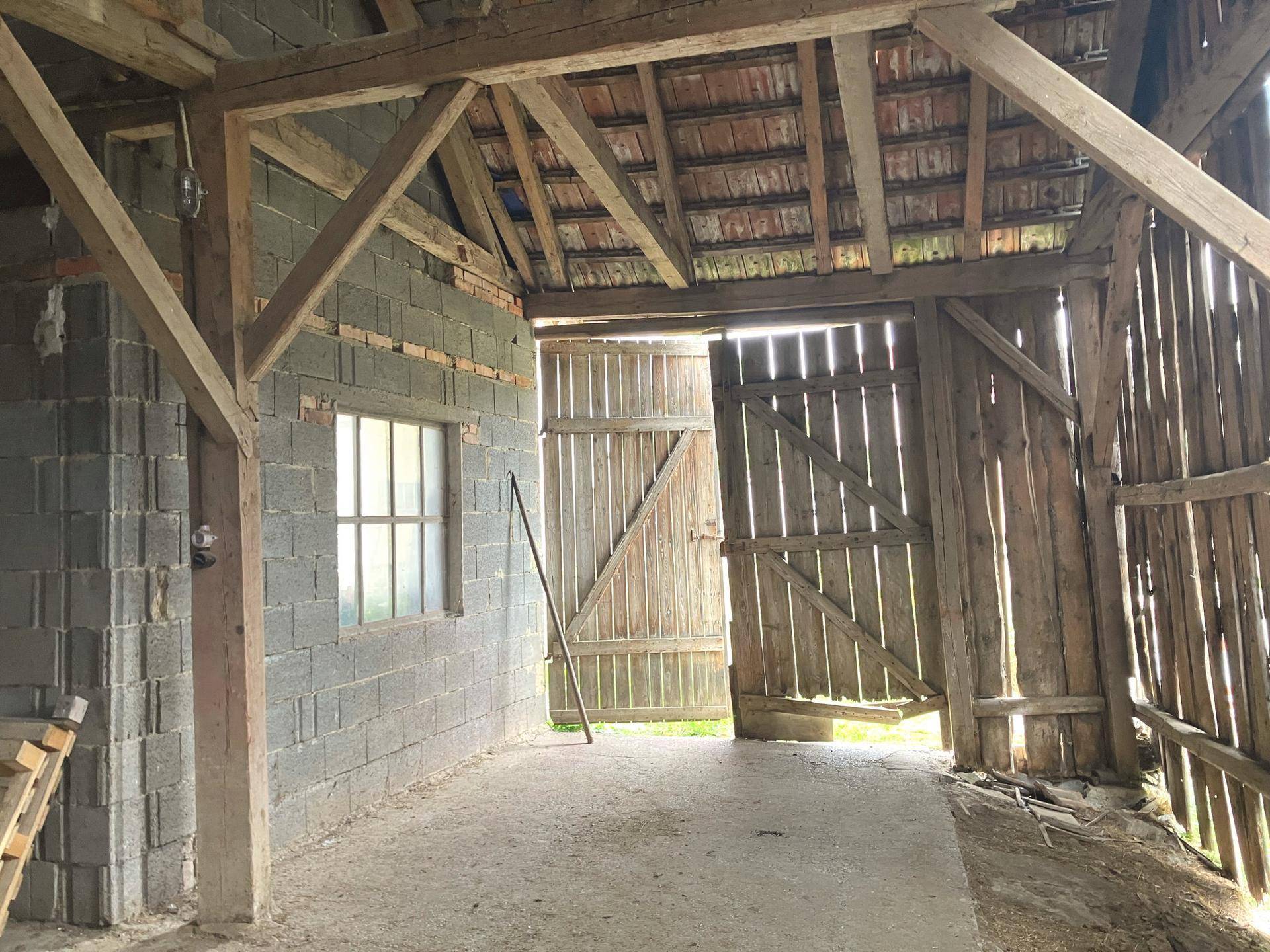 Geräumige Scheune mit sichtbarer Holzkonstruktion, Ziegelwänden und großen Holztoren.