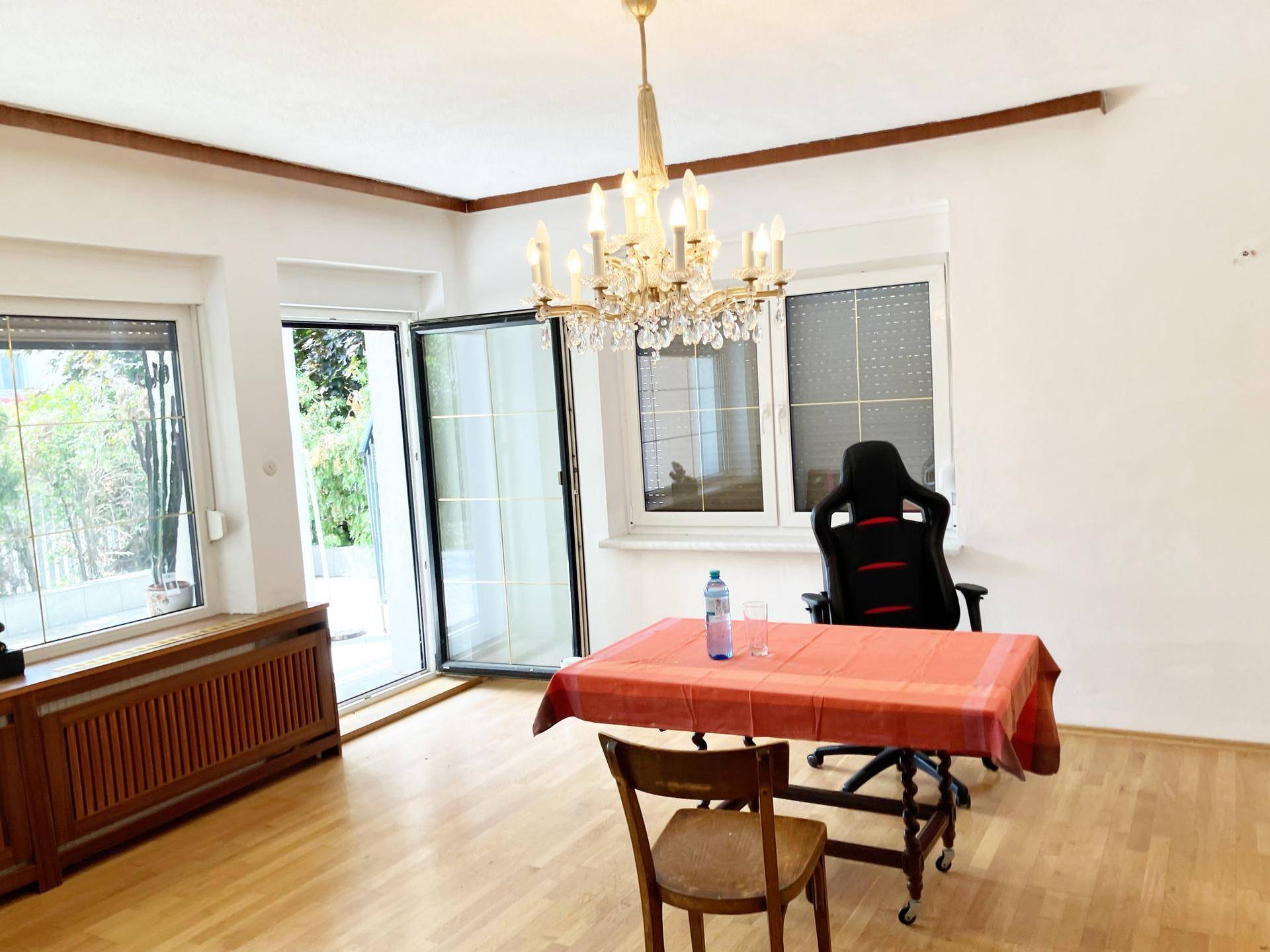 Geräumiges Wohnzimmer mit Kronleuchter, Holzboden und Zugang zu einem Außenbereich.