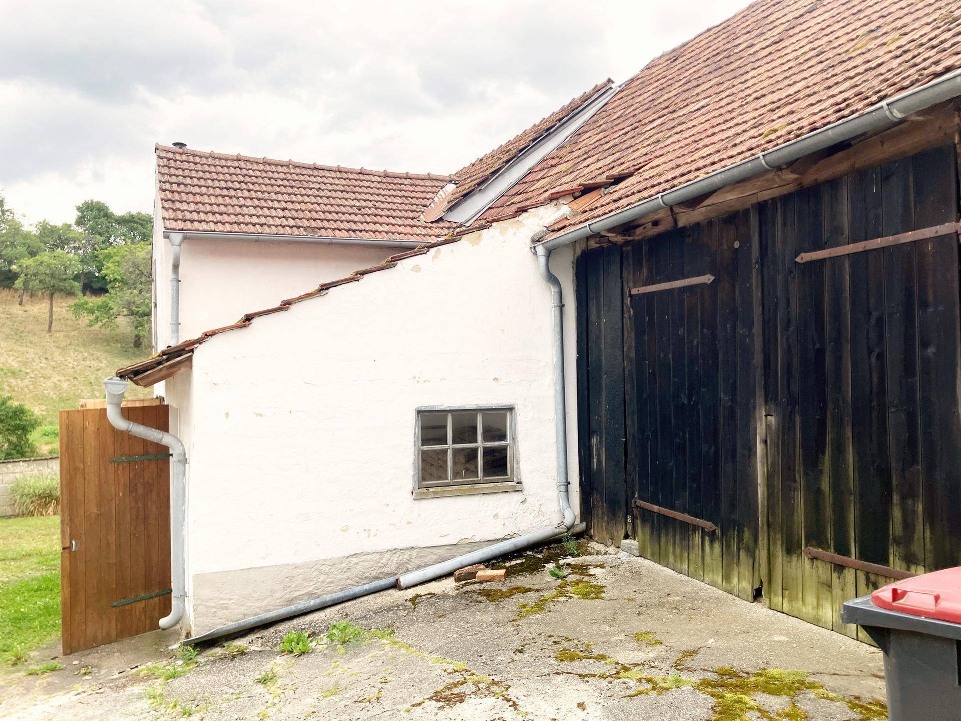 Seitenansicht eines ländlichen Gebäudes mit weißer Fassade und Holztüren.