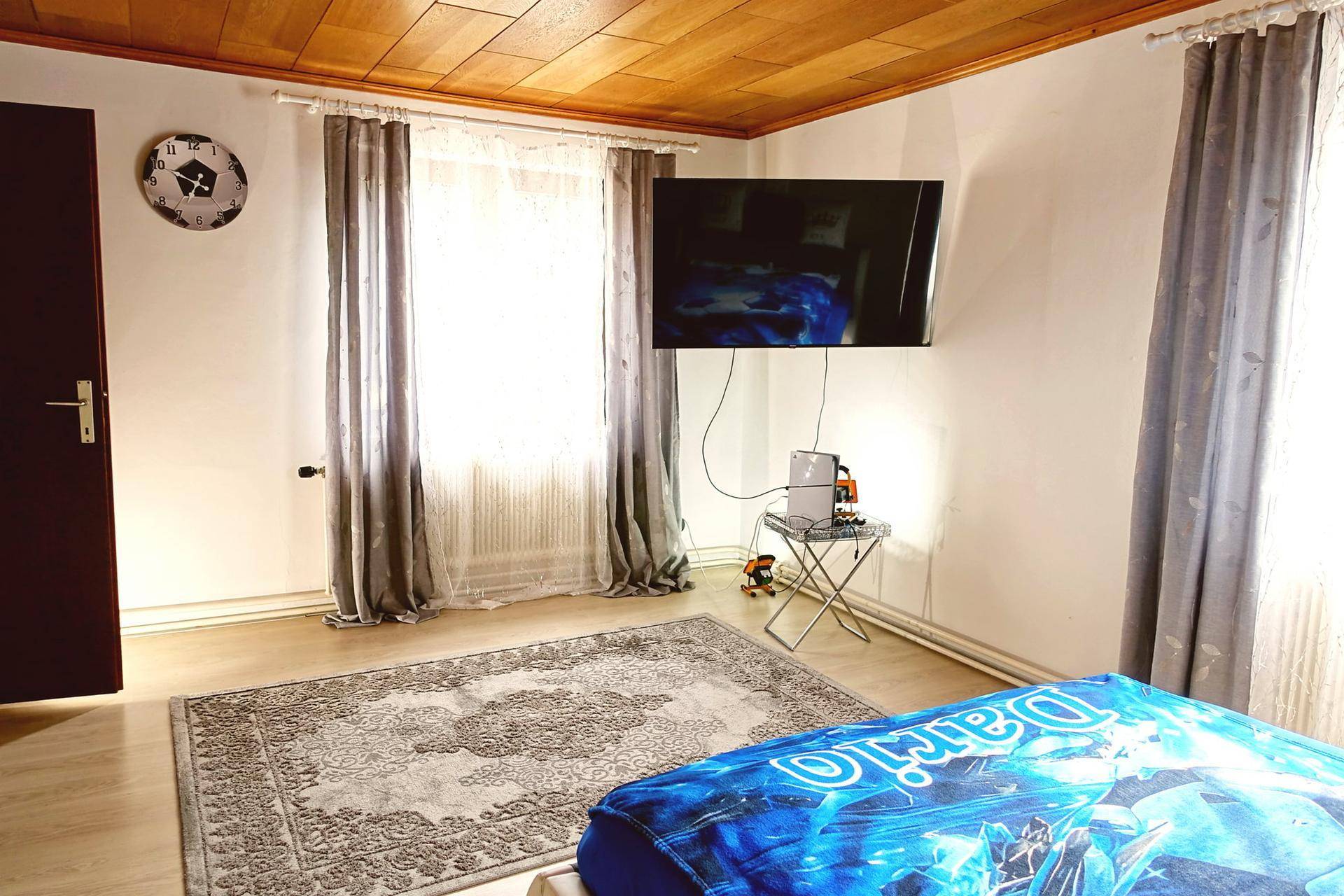 Schlafzimmer mit Doppelbett, Holzboden und einem an der Wand montierten Fernseher.