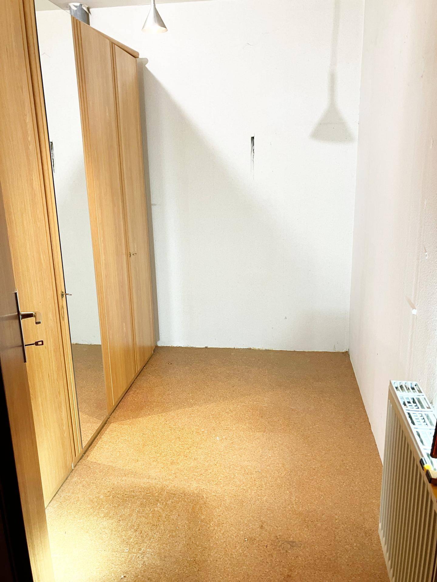 Schlafzimmer mit Korkboden, weiß gestrichenen Wänden und Spiegelschrank.