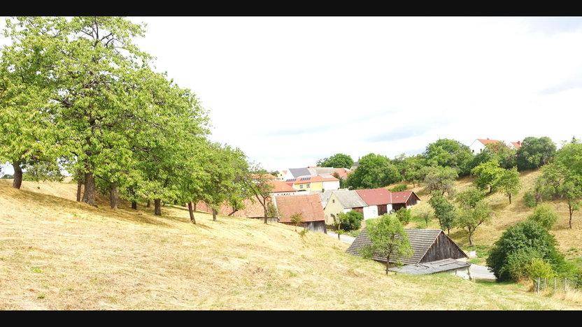 Panoramablick auf eine ländliche Siedlung mit Häusern und Bäumen in hügeliger Landschaft.