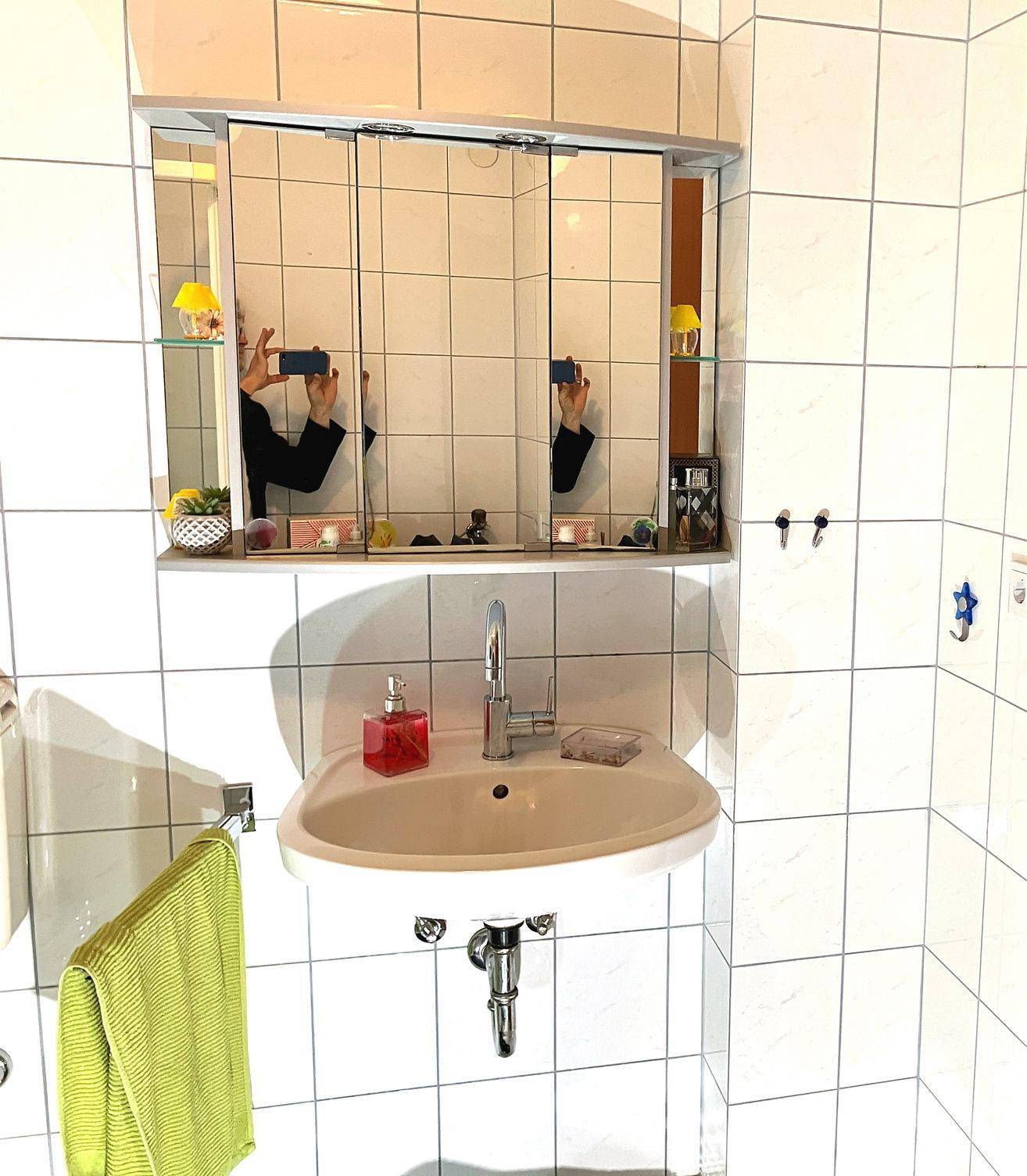 Kleines Badezimmer mit weiß gefliesten Wänden, Einzelwaschbecken und Spiegelschrank.