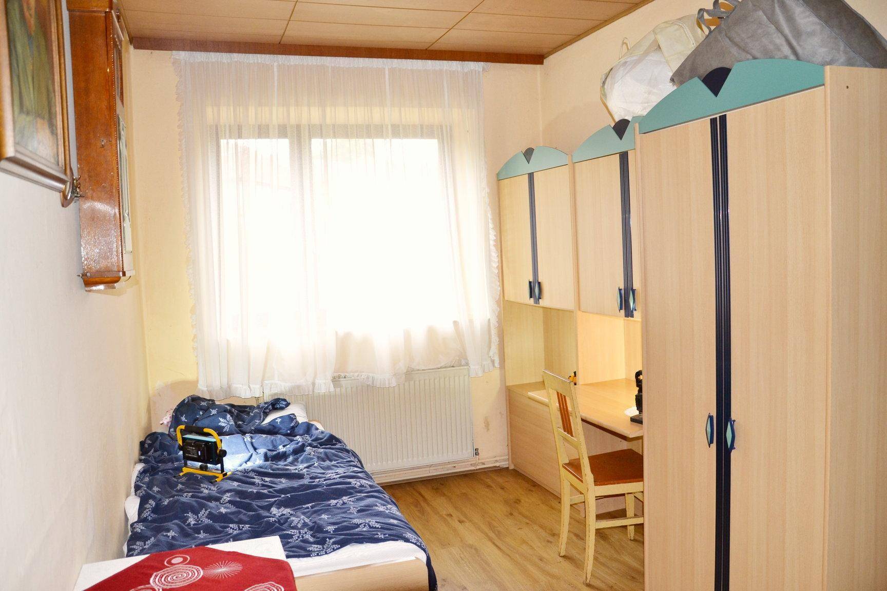 Schlafzimmer mit Einzelbett, Schreibtisch und Holzdecke.