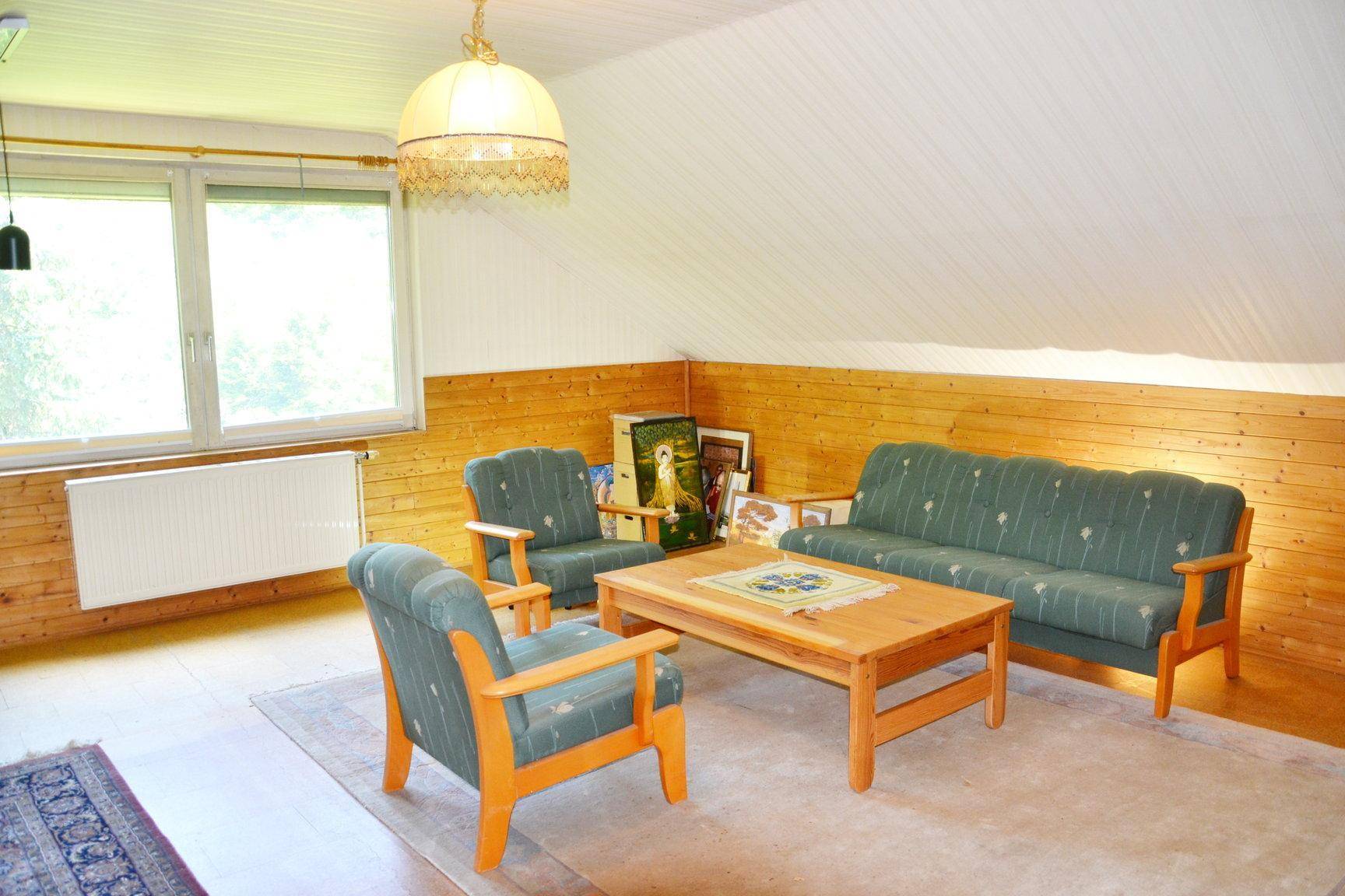Gemütliches Wohnzimmer im Dachgeschoss mit Schrägen, Holzvertäfelung und Sitzmöbeln.