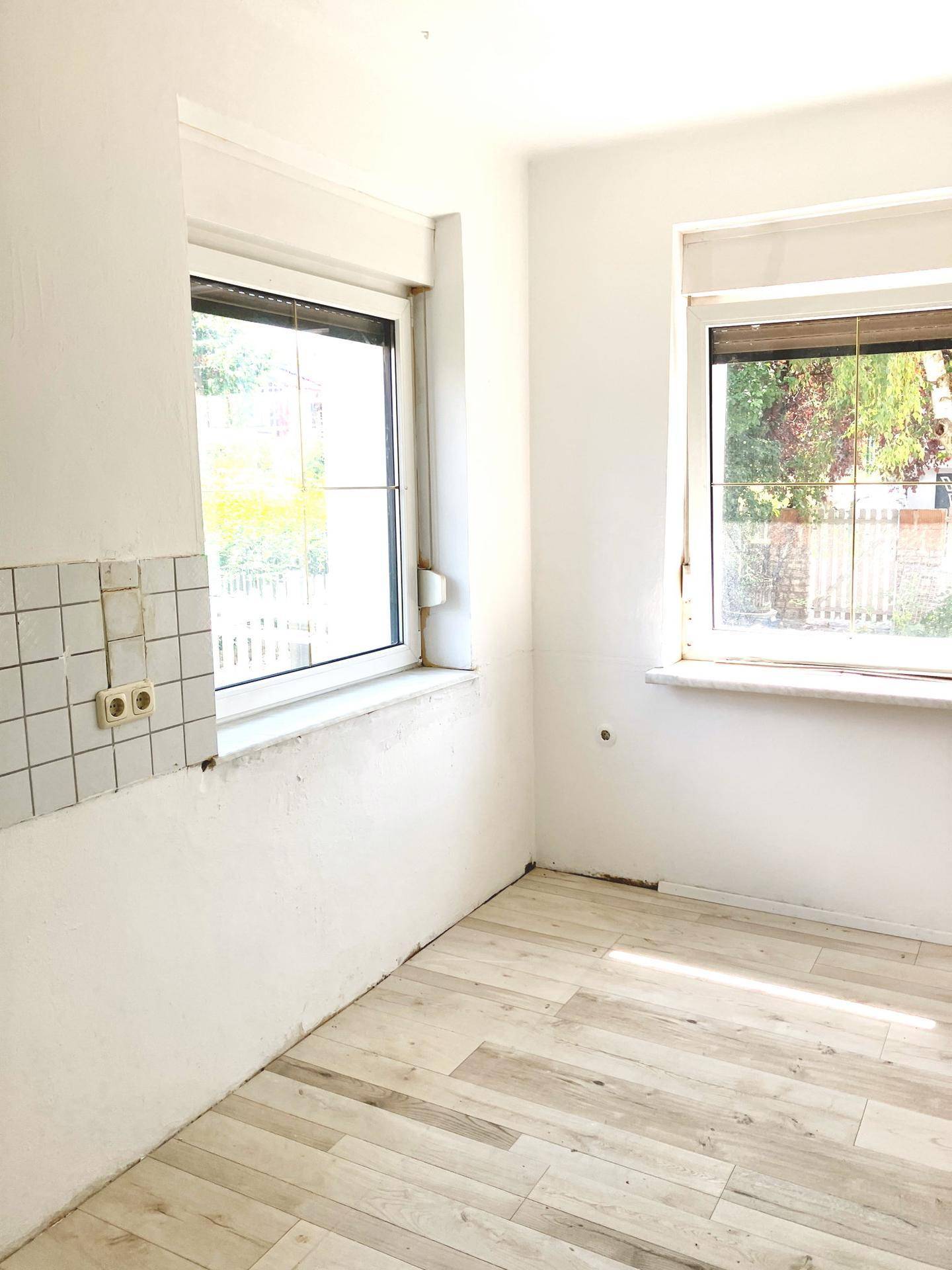 Heller Küchenraum mit zwei Fenstern und hellem Laminatboden, bereit für die Kücheninstallation.