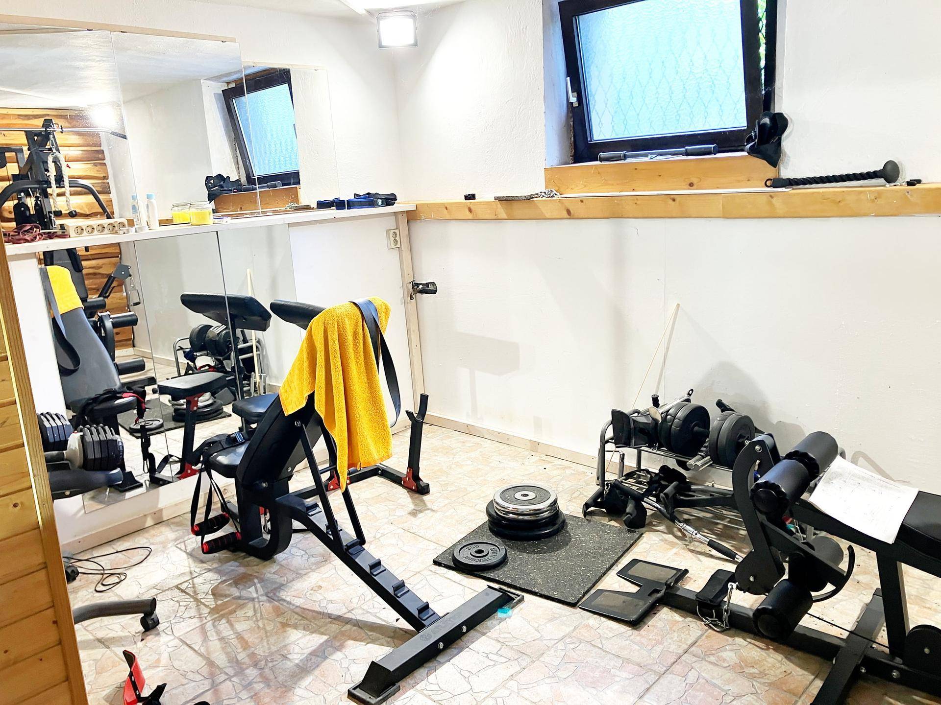 Fitnessraum im Keller mit verschiedenen Trainingsgeräten und Spiegelfront.