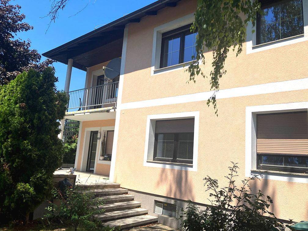 Seitenansicht des Hauses mit Balkon, Außentreppe und Rollläden an den Fenstern.