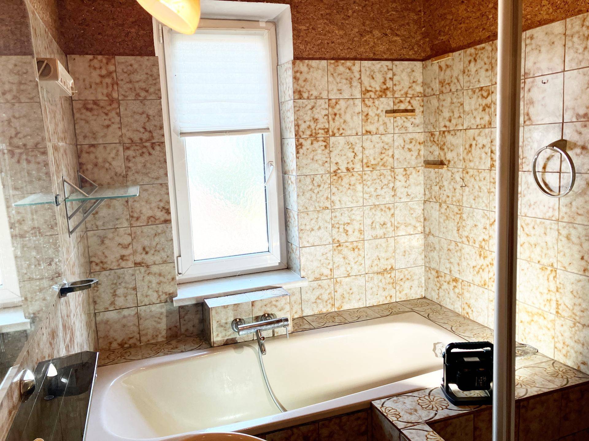 Badezimmer mit Badewanne, gefliesten Wänden und Fenster für Tageslicht.