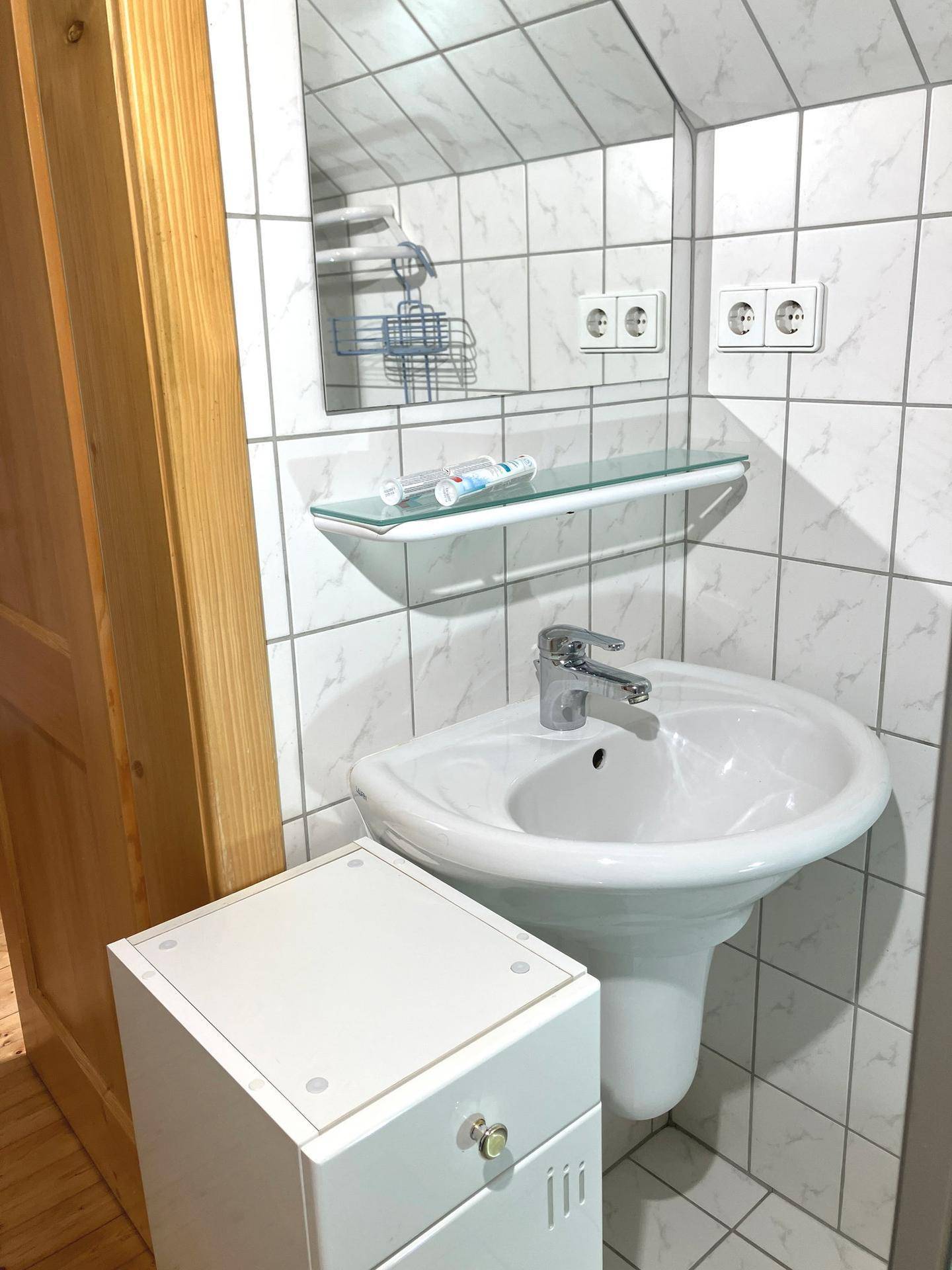 Kleines Badezimmer mit Waschbecken, Spiegel und weißen Wandfliesen.