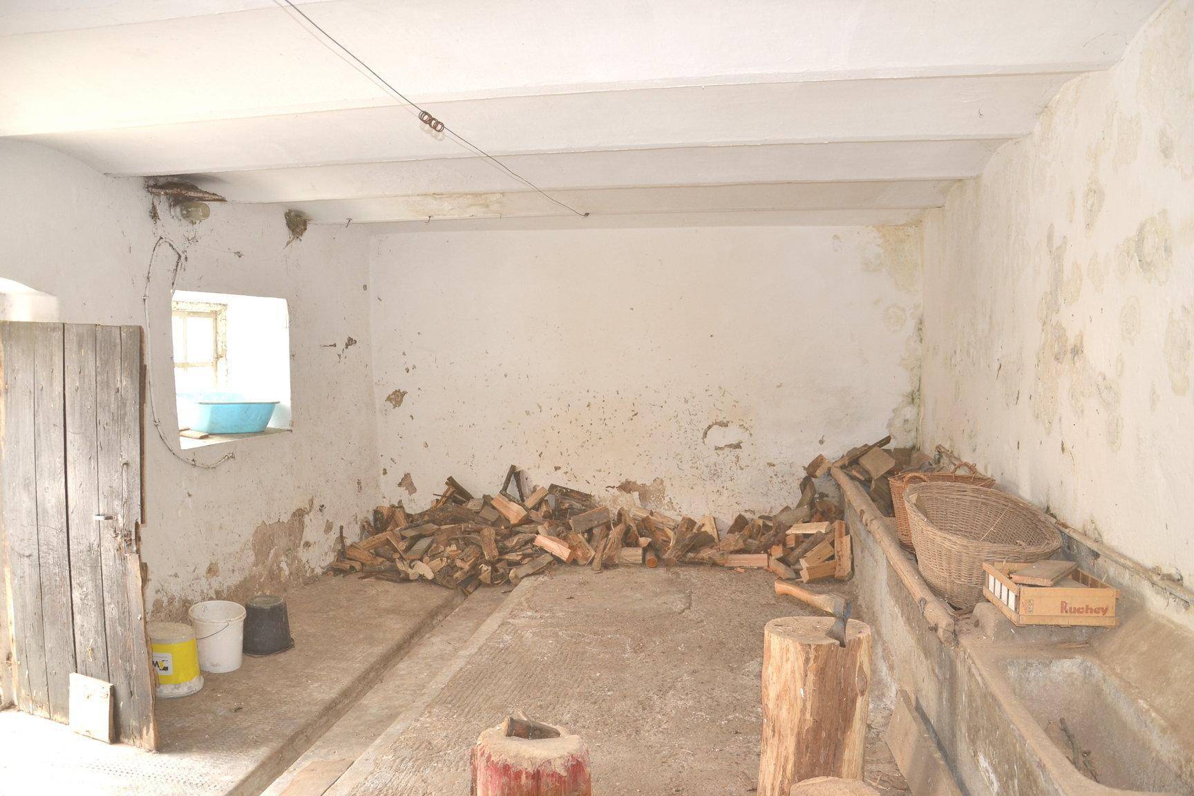 Rustikaler Lagerraum mit Holzbalkendecke, gestapeltem Brennholz und alten Trögen.