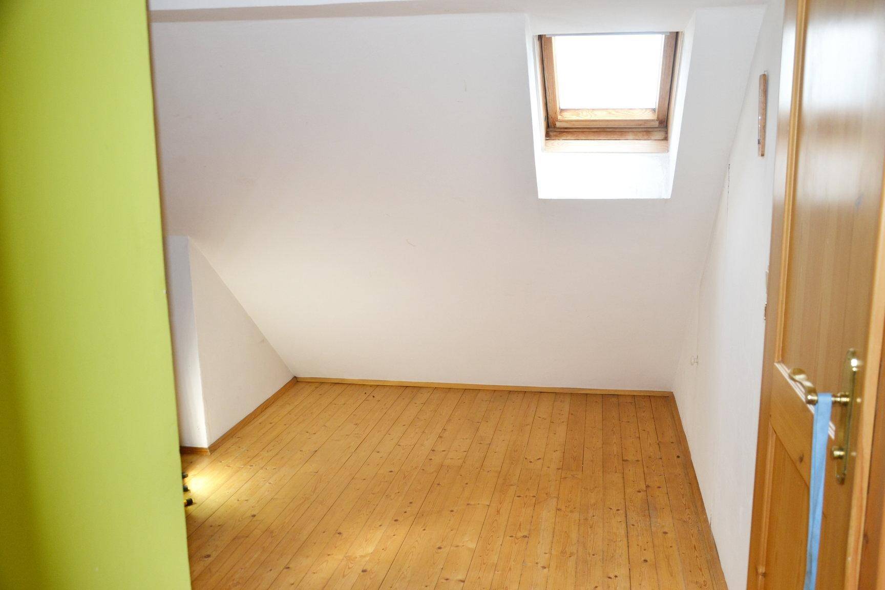 Dachzimmer mit Holzdielenboden, weiß gestrichenen Wänden und Dachfenster.
