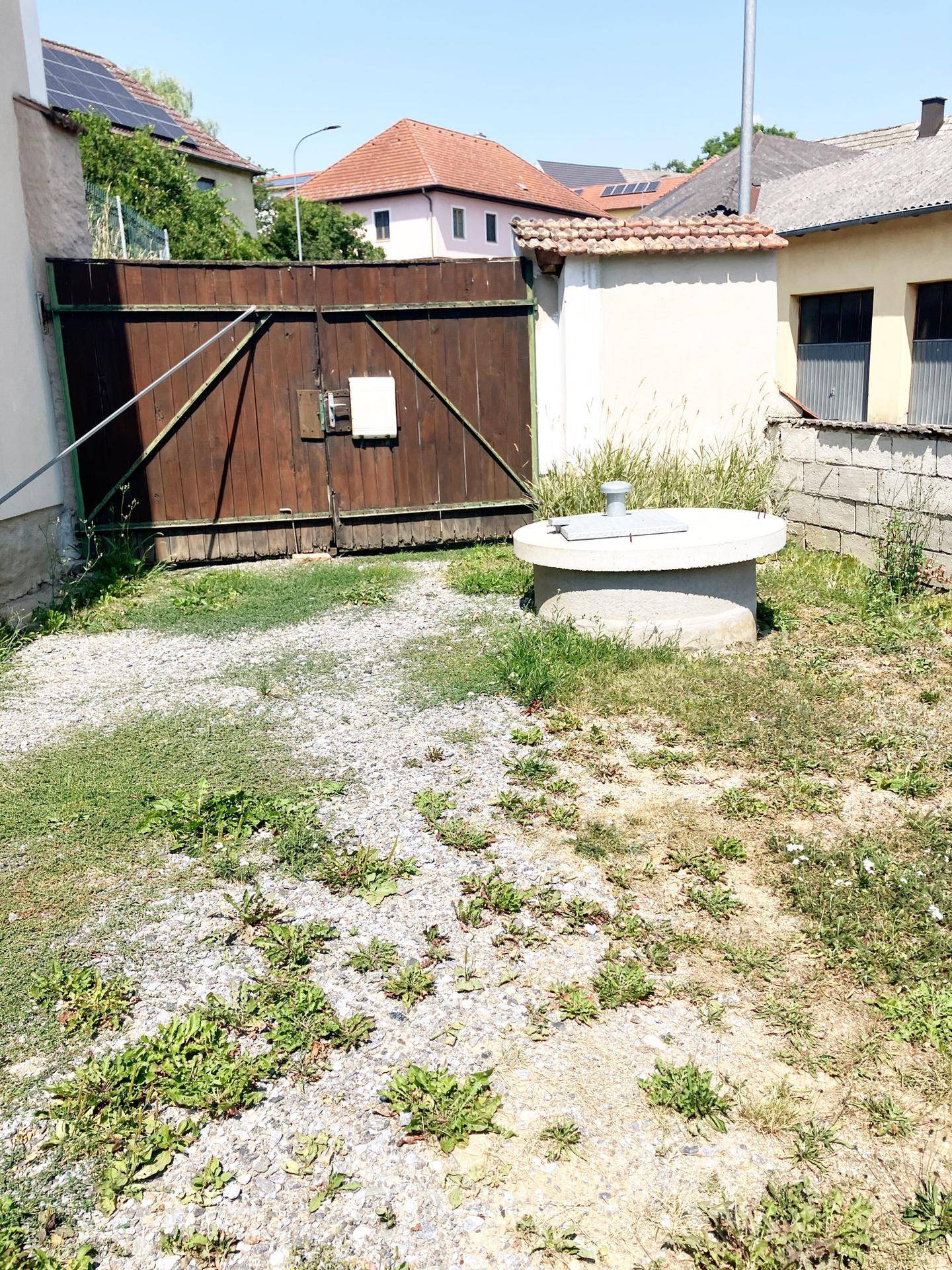 Hinterhofbereich mit Brunnen und Holztor.