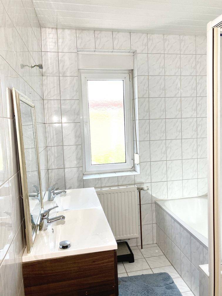 Badezimmer mit weißen Fliesen, Doppelwaschbecken, Spiegel und einer Badewanne.