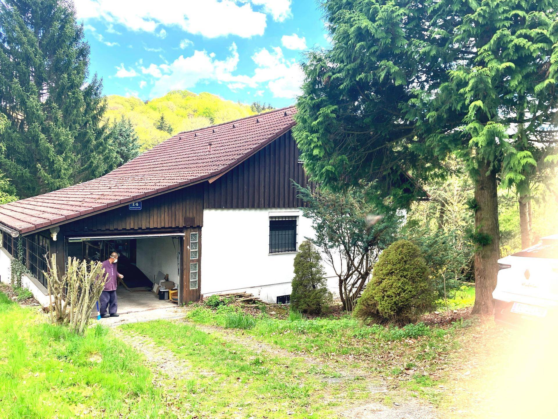 Ansicht des Hauses mit Garage, umgeben von Bäumen und viel Grün.