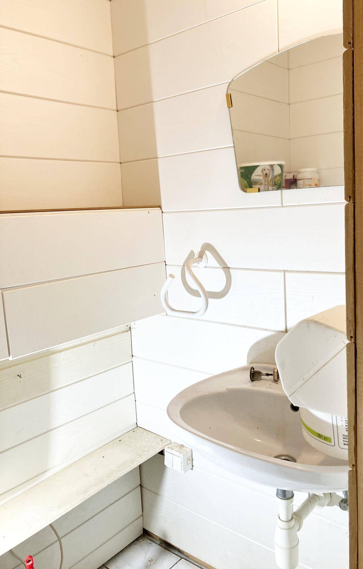 Kleiner Waschraum mit Waschbecken, Spiegel und Holzvertäfelung.