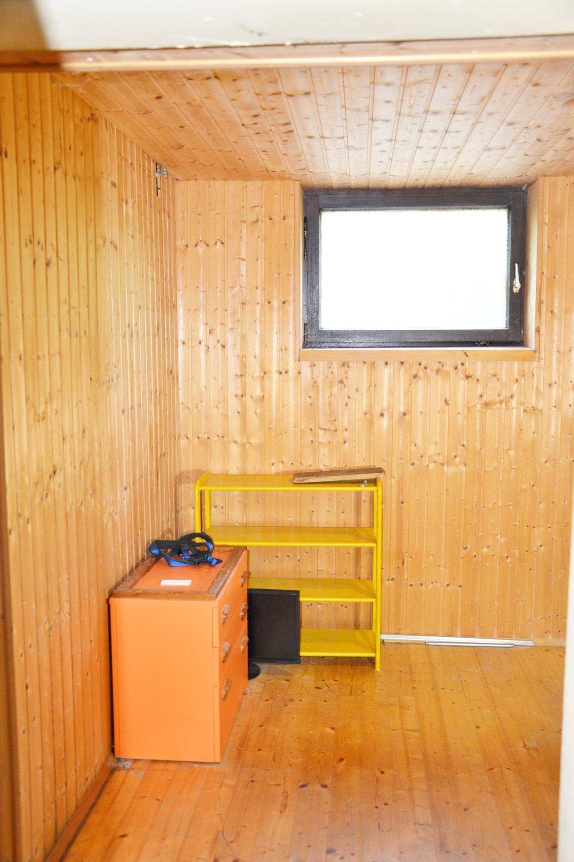 Holzvertäfeltes Zimmer mit Fenster, Holzboden und gelbem Regal.