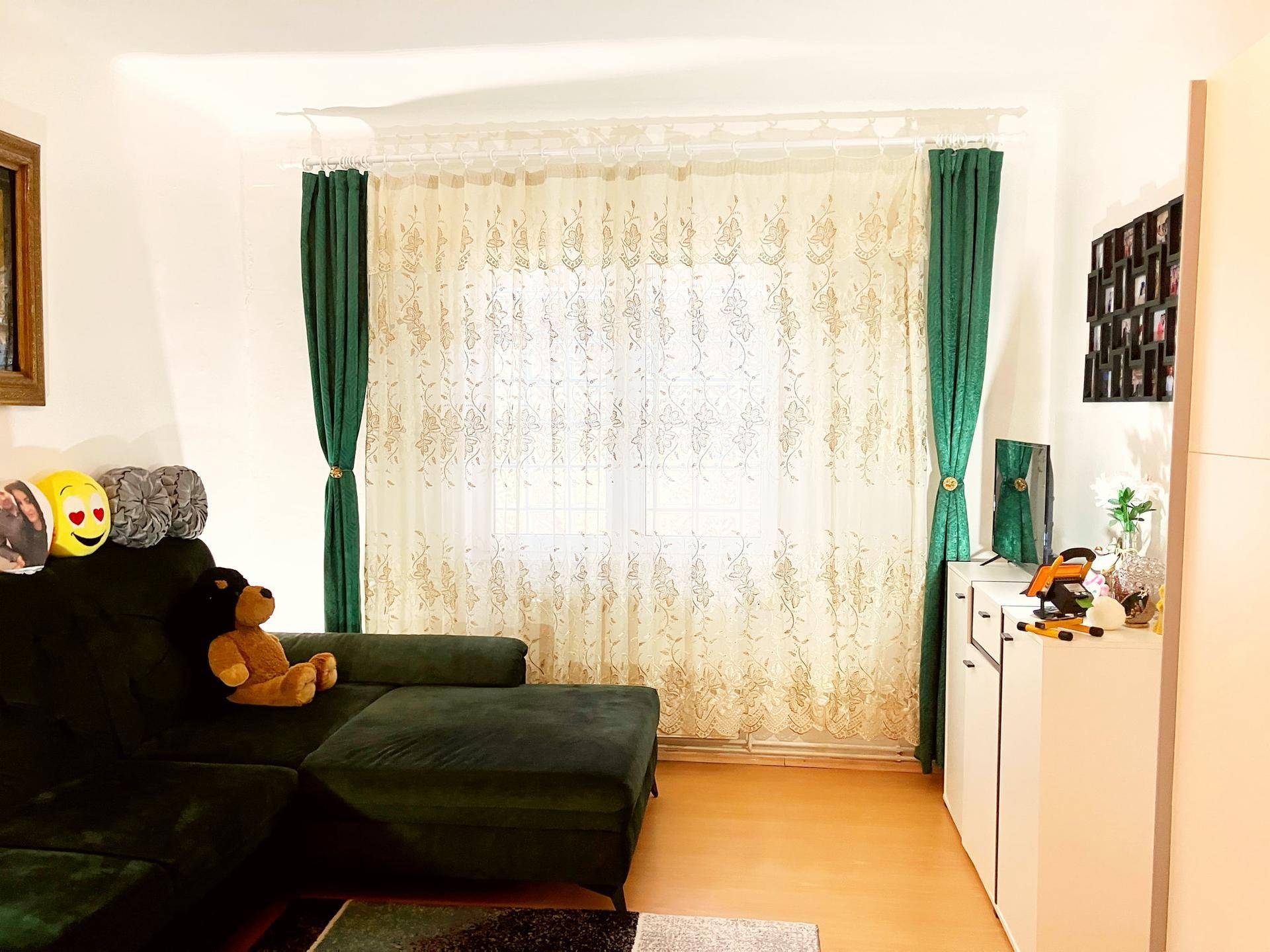 Gemütliches Wohnzimmer mit dunkelgrünem Ecksofa, hellem Holzboden und großen Fenstern.