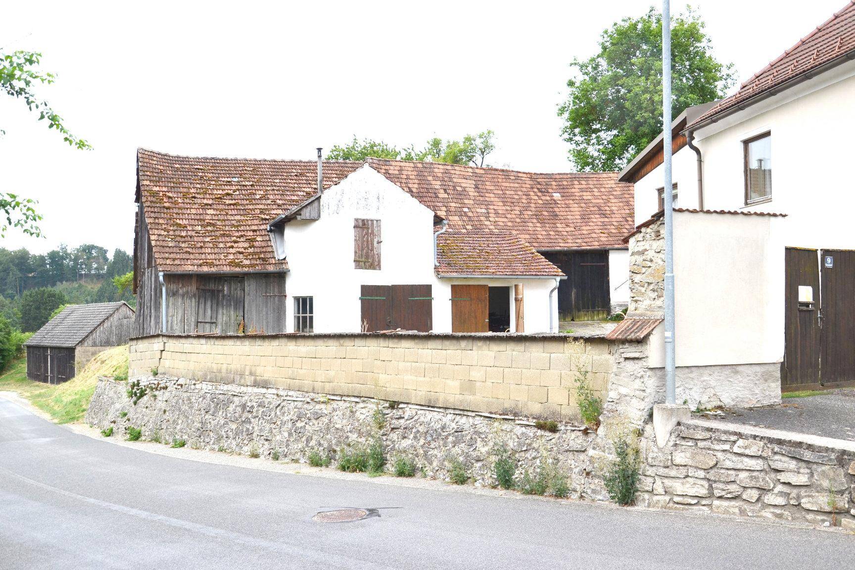 Ländliche Straße mit mehreren alten Gebäuden, Ziegeldächern und einer Steinmauer.