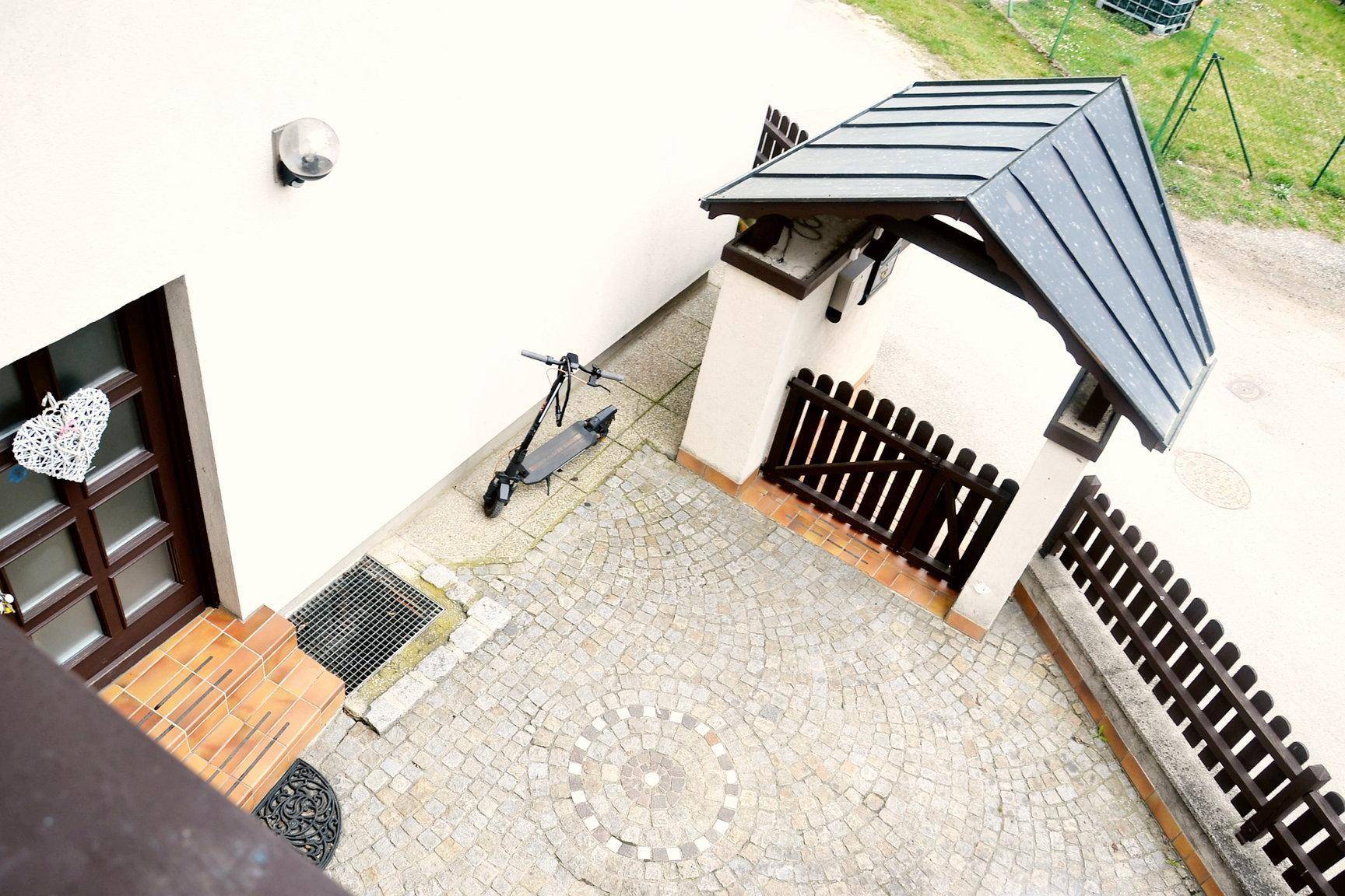 Gepflasterter Hofbereich mit überdachtem Eingang und Zaun, bietet Platz für einen Roller.