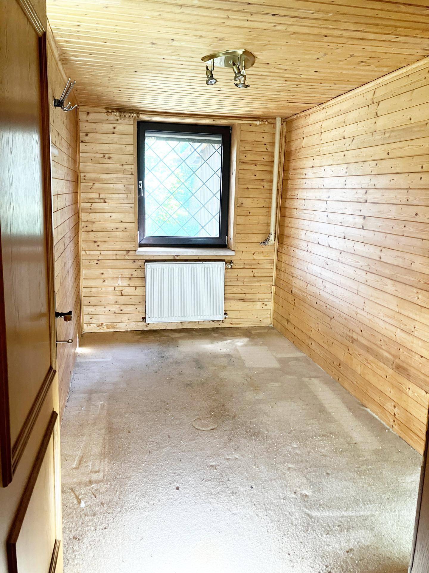 Leerer Raum mit Holzverkleidung, einem Fenster und einem Heizkörper unter dem Fenster.