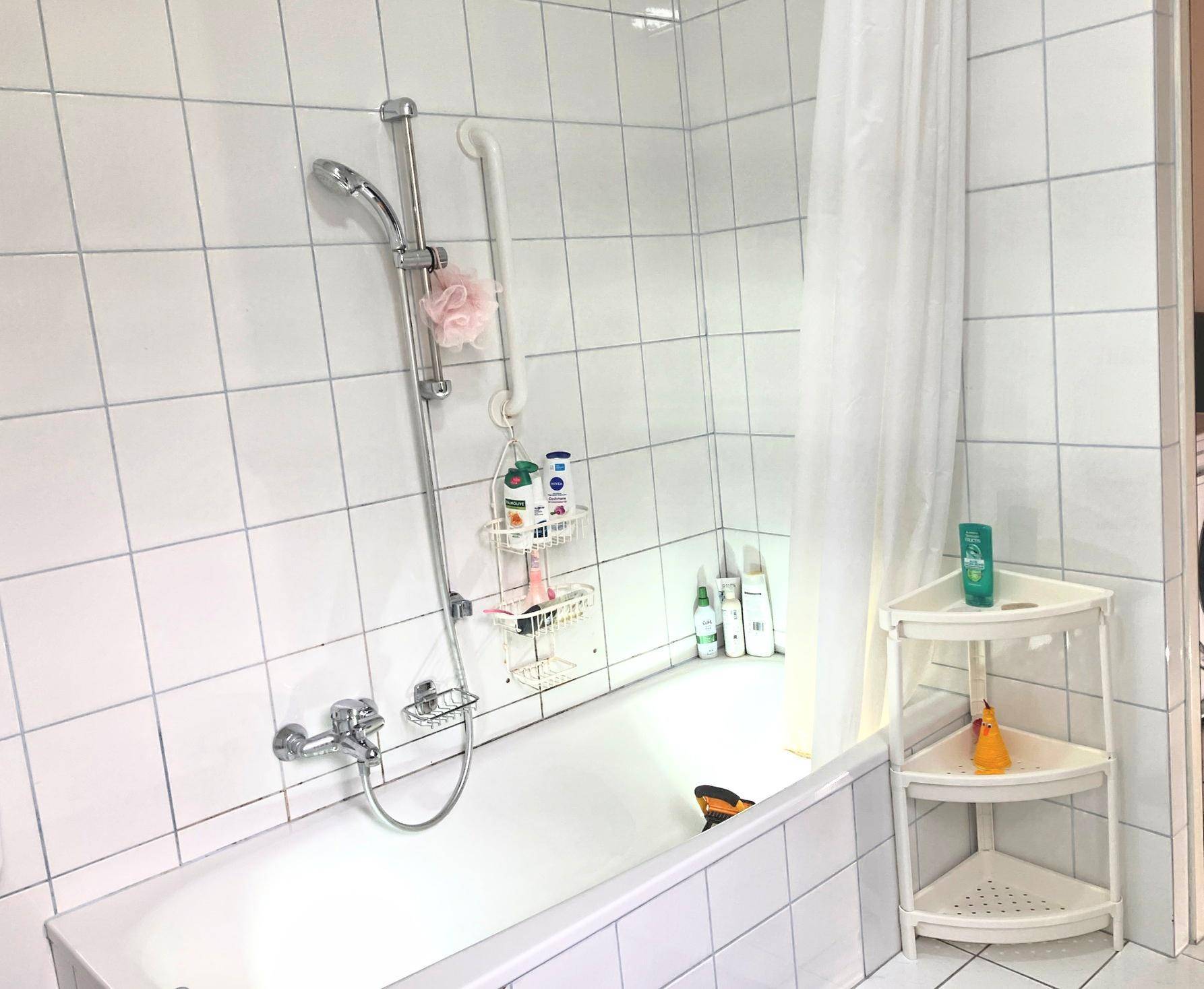 Badezimmer mit Badewanne, Duschvorhang und weißen Wandfliesen.